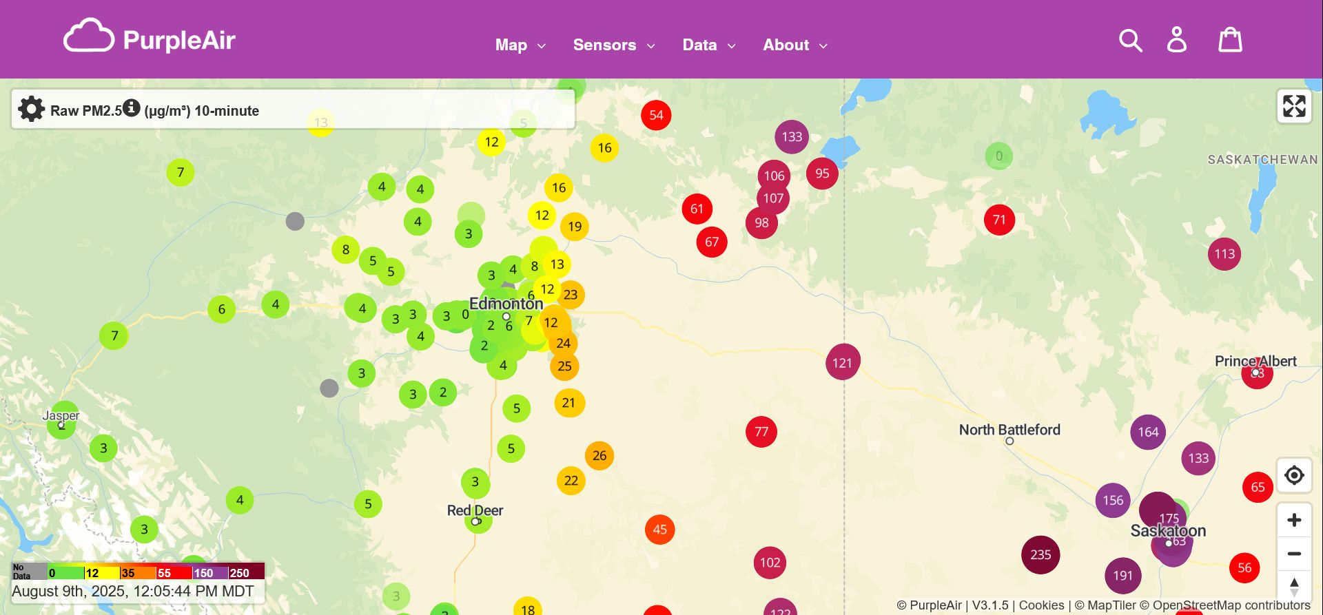 Screenshot of the Purple Air real time map of Raw PM2.5 levels, showing central Alberta and parts of Saskatchewan, at 12:05 MDT. Most of the Edmonton area is covered in bright green data point dots, with readings under 5 micrograms per cubic meter. The eastern edge of the metropolitan area, however, transitions to yellow and orange (readings in the 20s). Data points are less frequent outside the city, but as we continue east they switch to red, purple, and maroon brown, with correspondingly higher readings. Some stations near Saskatoon have particulate levels around 200 micrograms per meter cubed.
