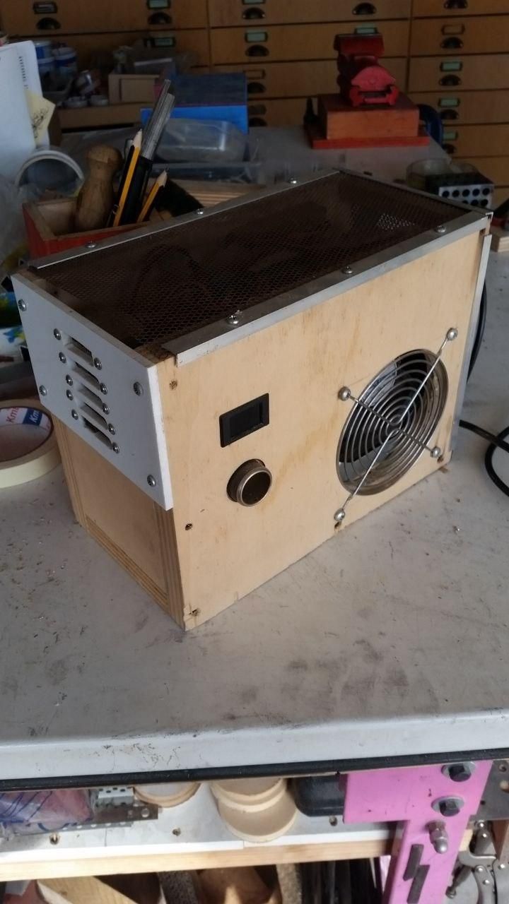 Alimentatore AT in cassetta di compensato autocostruita, con 10 porte USB sul lato corto, e un voltmetro, una persa 12V tipo accendisigari da auto e una ventola sul lato lungo.
Sopra c'è una griglia per la ventilazione.