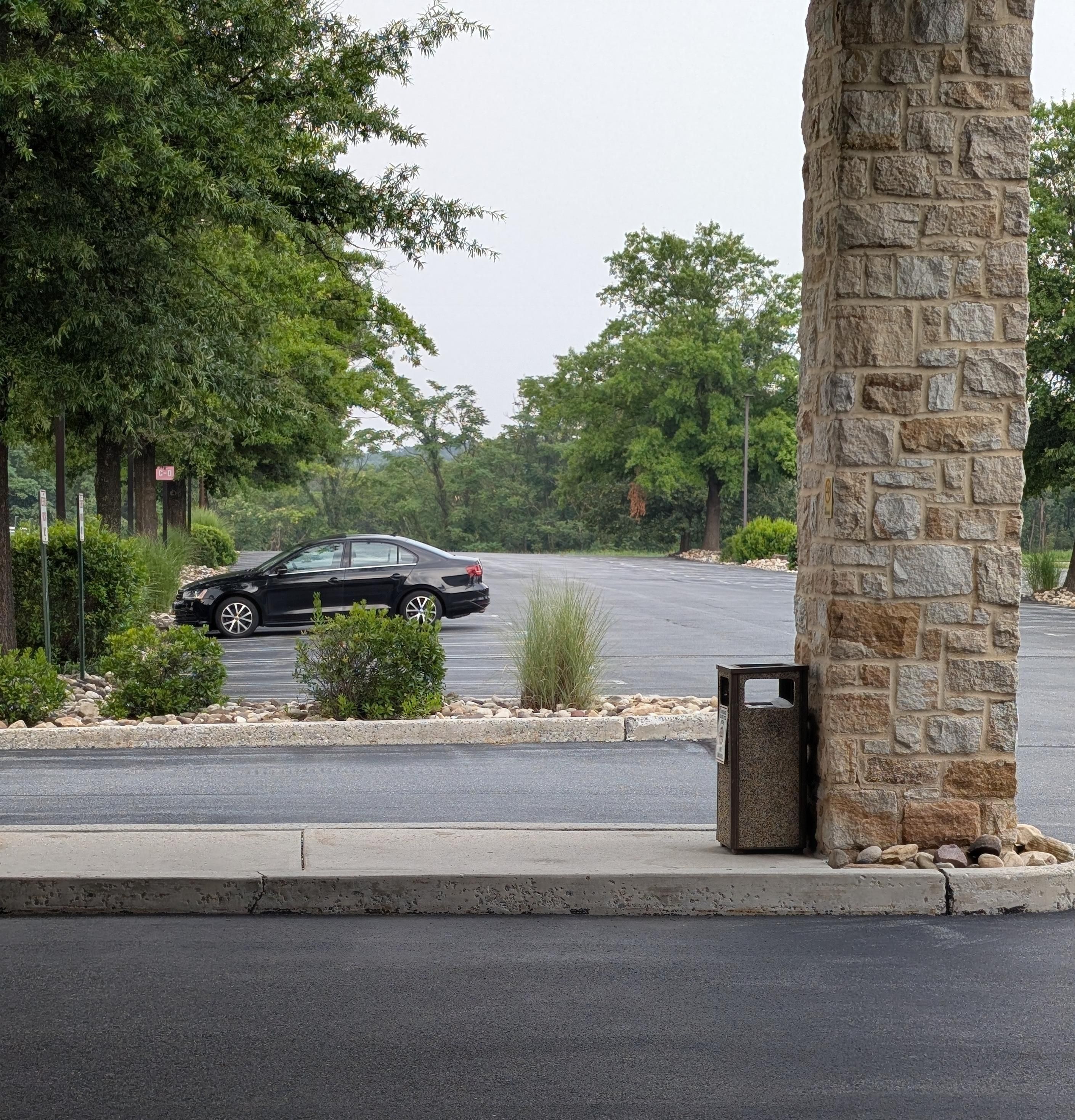 A picture of one lone black Volkswagen sedan off in the distance in an empty corporate office parking lot.