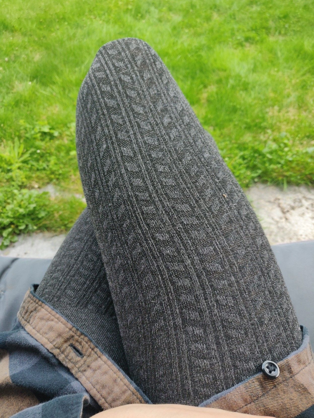 Photo of my crossed legs in dark grey leggings, sitting in the garden so there's green grass in the background. My upper thighs are covered by a blue and brown flannel shirt