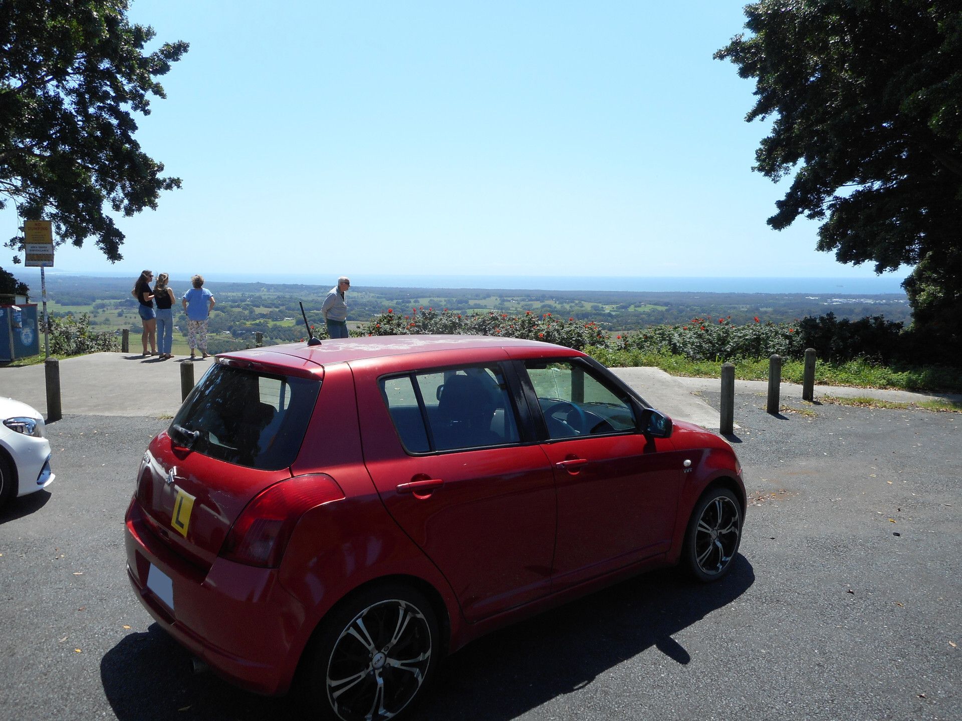 A red Suzuki Swift, parked in nearly the same spot as the ZZR. Notable details include the large CSA rims and some paint sunburn.