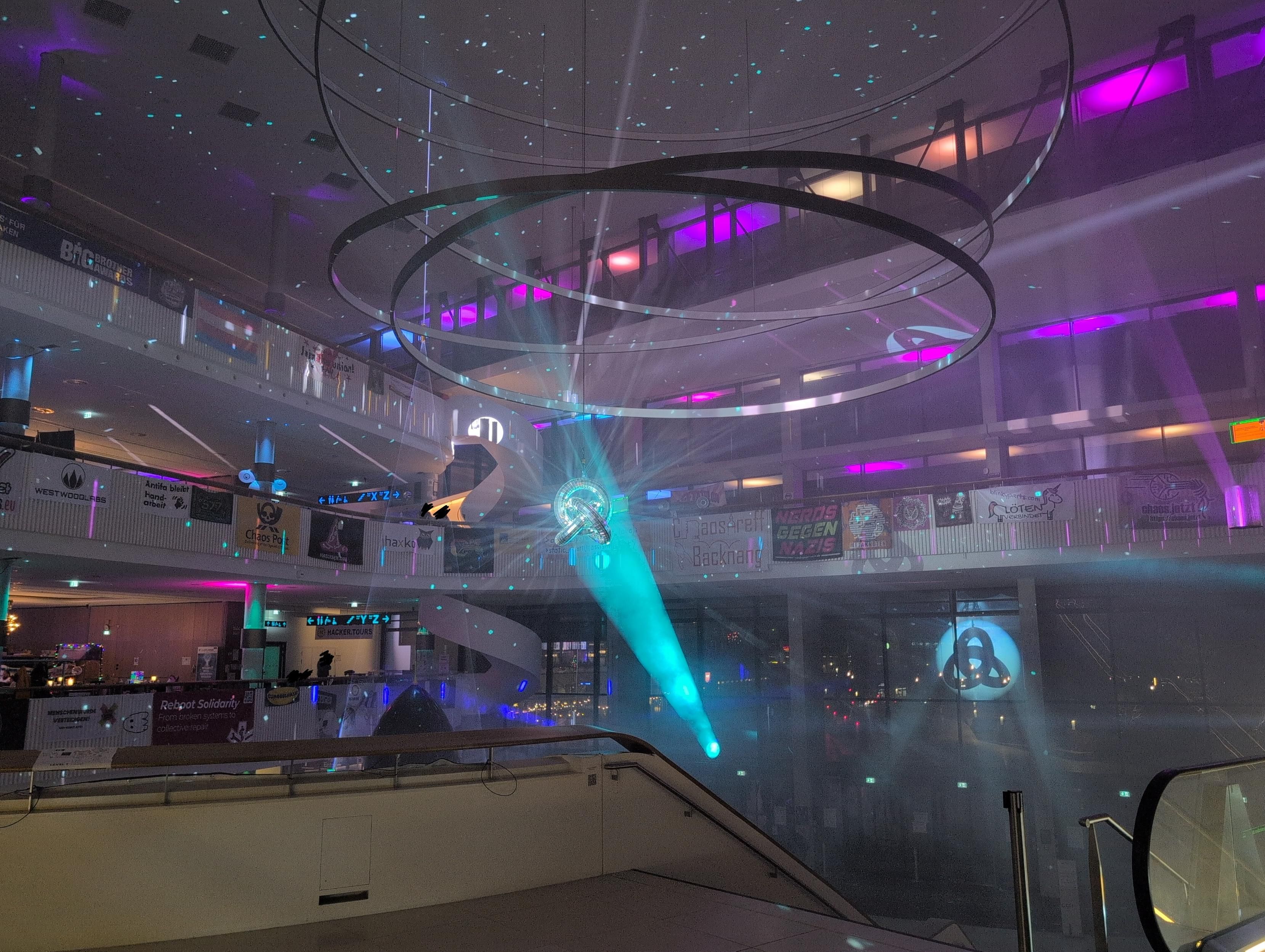 Photo of a tall entrance foyer at a fair. From the ceiling hangs a disco knot, spreading blue light from a spotlight ibto hundreds of little spots.

A handful of tiny human silhouettes are scribbled over (I did not notice them when taking the photo).