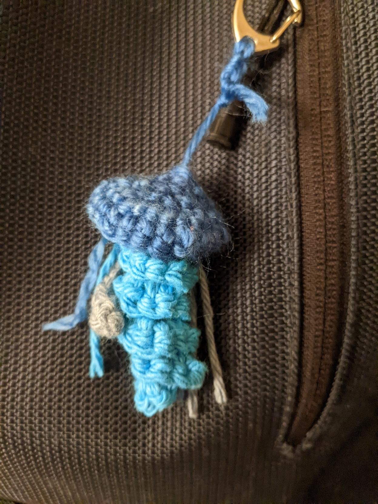 A crocheted blue and pale purple jellyfish against a bag