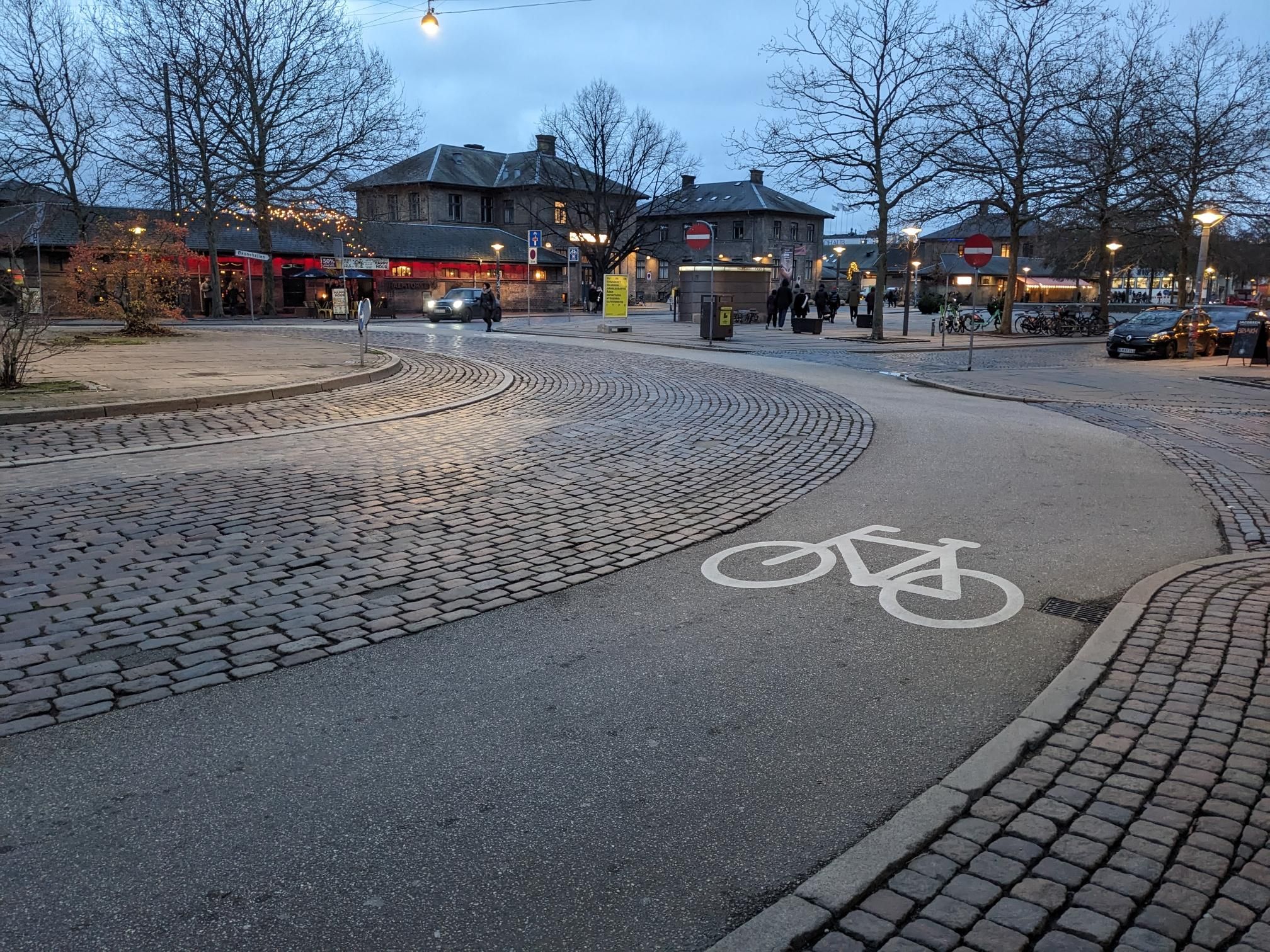 Thinner asphalt roundabout with a bike symbol. Inside, there's more cobblestone street.