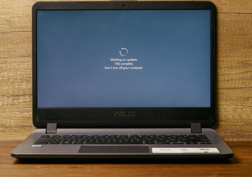 A photo of a laptop sitting on a wooden table with the message "working on updates, 15 percent complete. Do not turn off your computer."