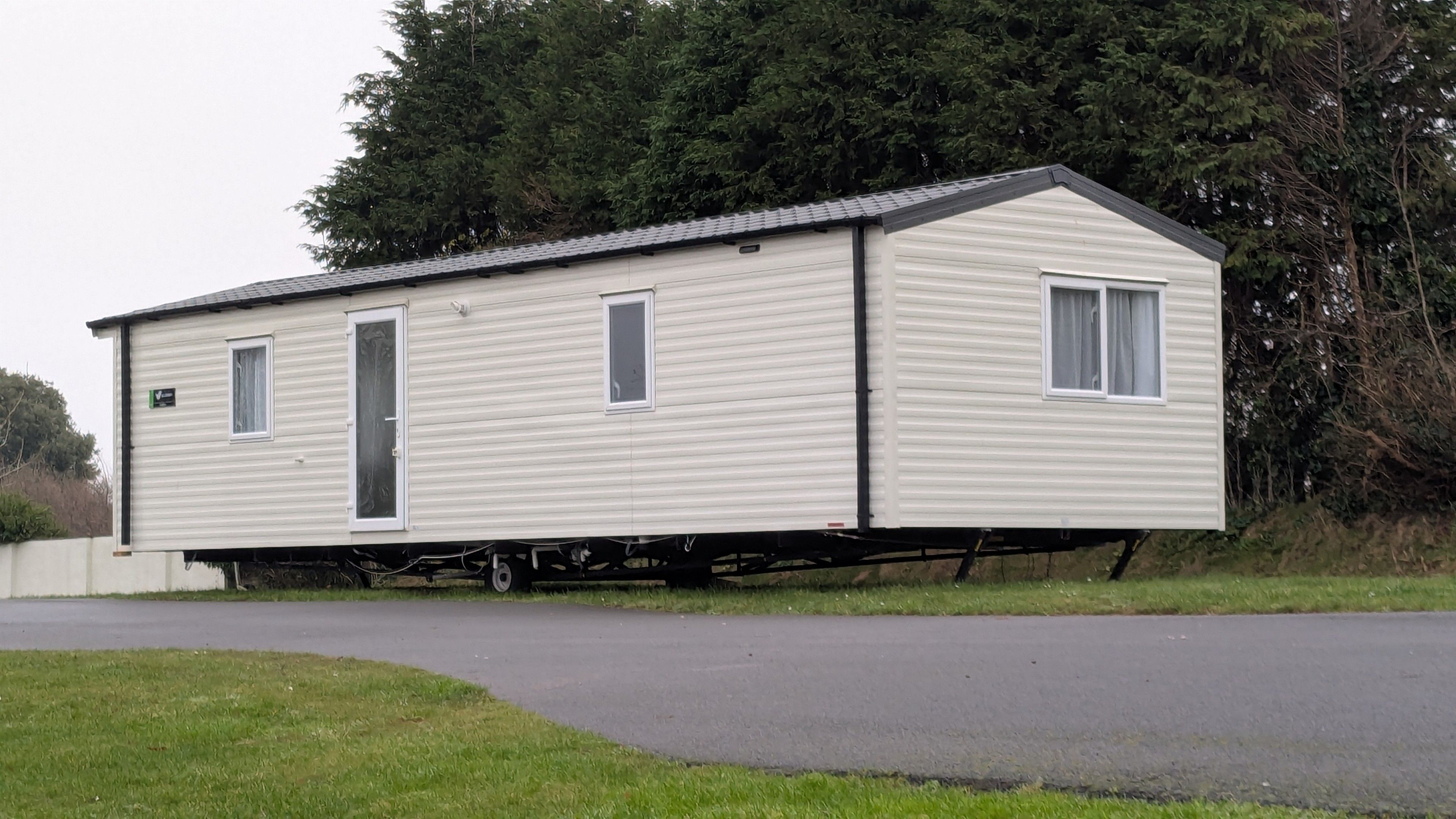 Ein weißer static caravan. Zubsehen ist die lange Seite mit der Eingangstür und eine kurze Seite. Er ist noch nicht fest  aufgestellt und steht auf den eigenen Rädern. Er sieht aus wie ein kleines Haus.