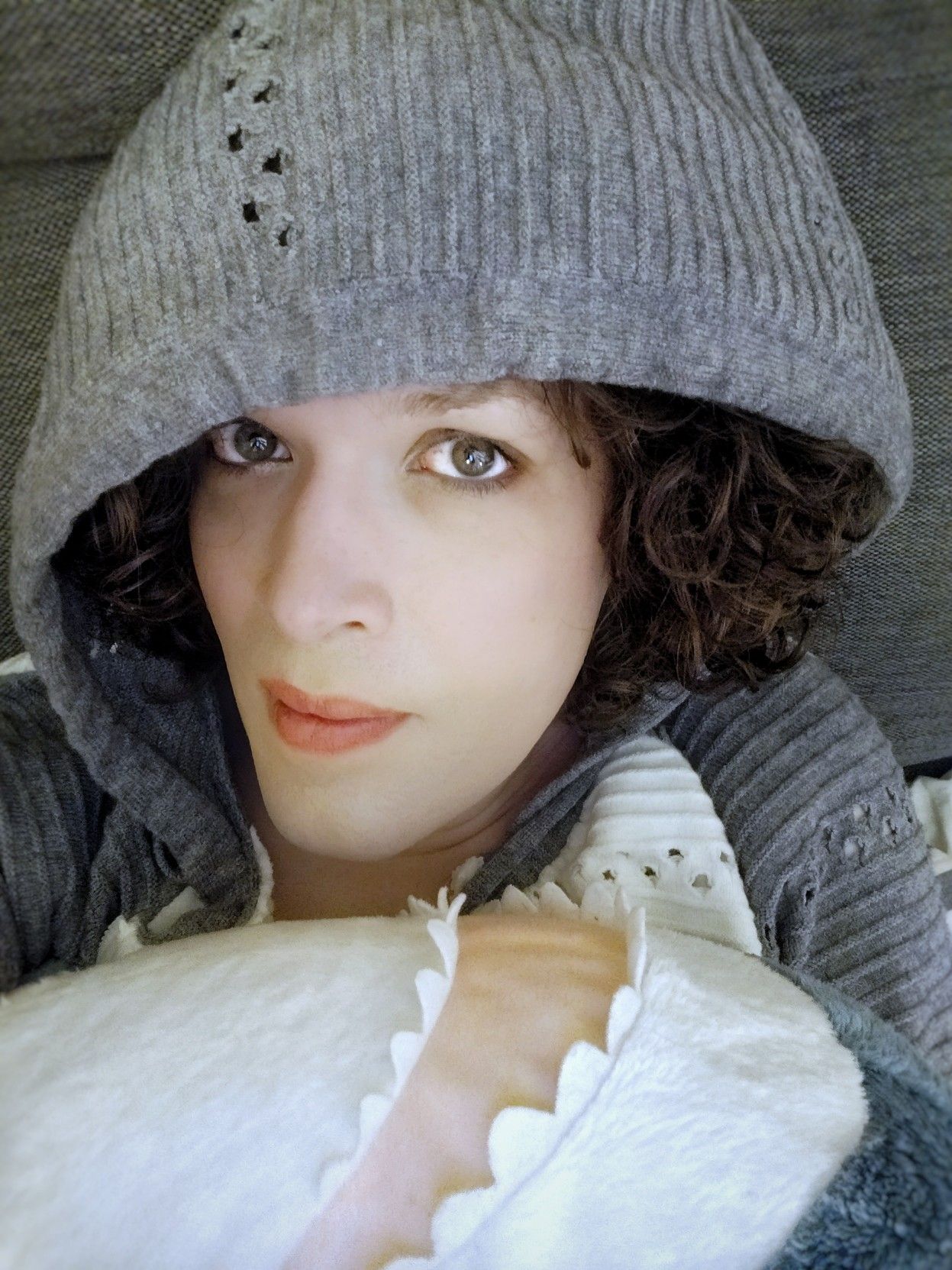 me in a grey hood, smiling and looking up at the camera, holding a blåhaj plushie belly up right under my chin