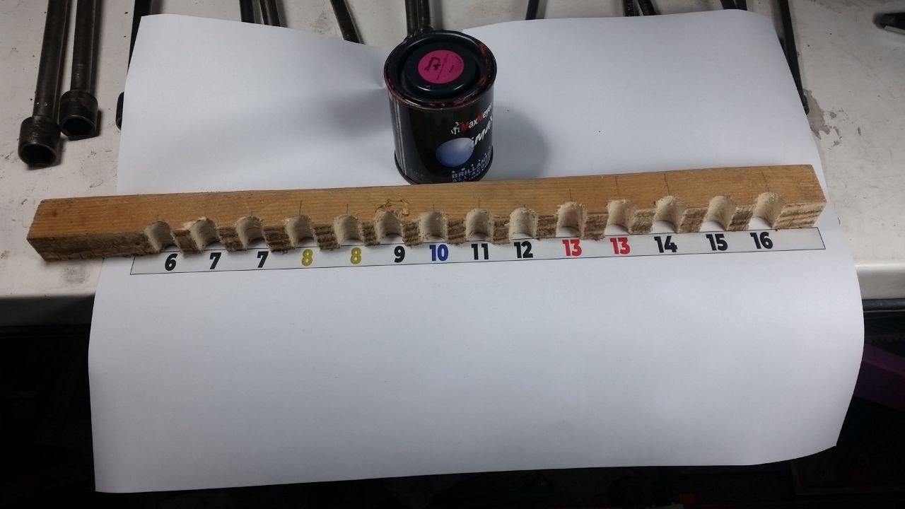 Foglio A4 con stampata una serie di numeri, da 6 a 16, sul quale e poggiato uno dei lati del supporto per chiavi a T.
Dietro un barattolino di smalto all'acqua Max Meyer color fucsia.