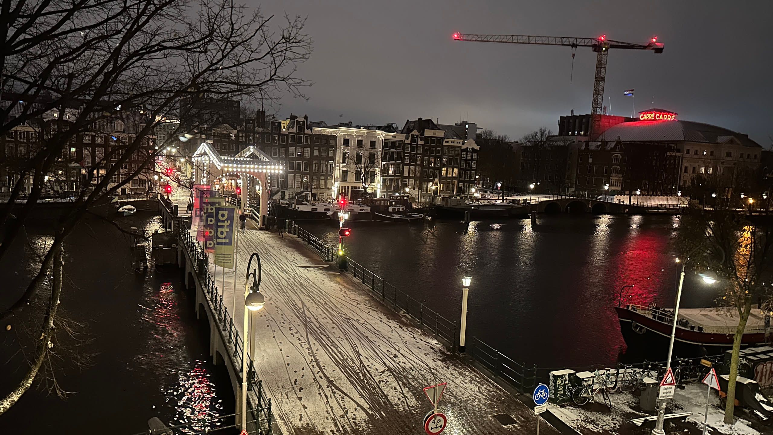 snowy bridge across a river at night with a work crane above a theater