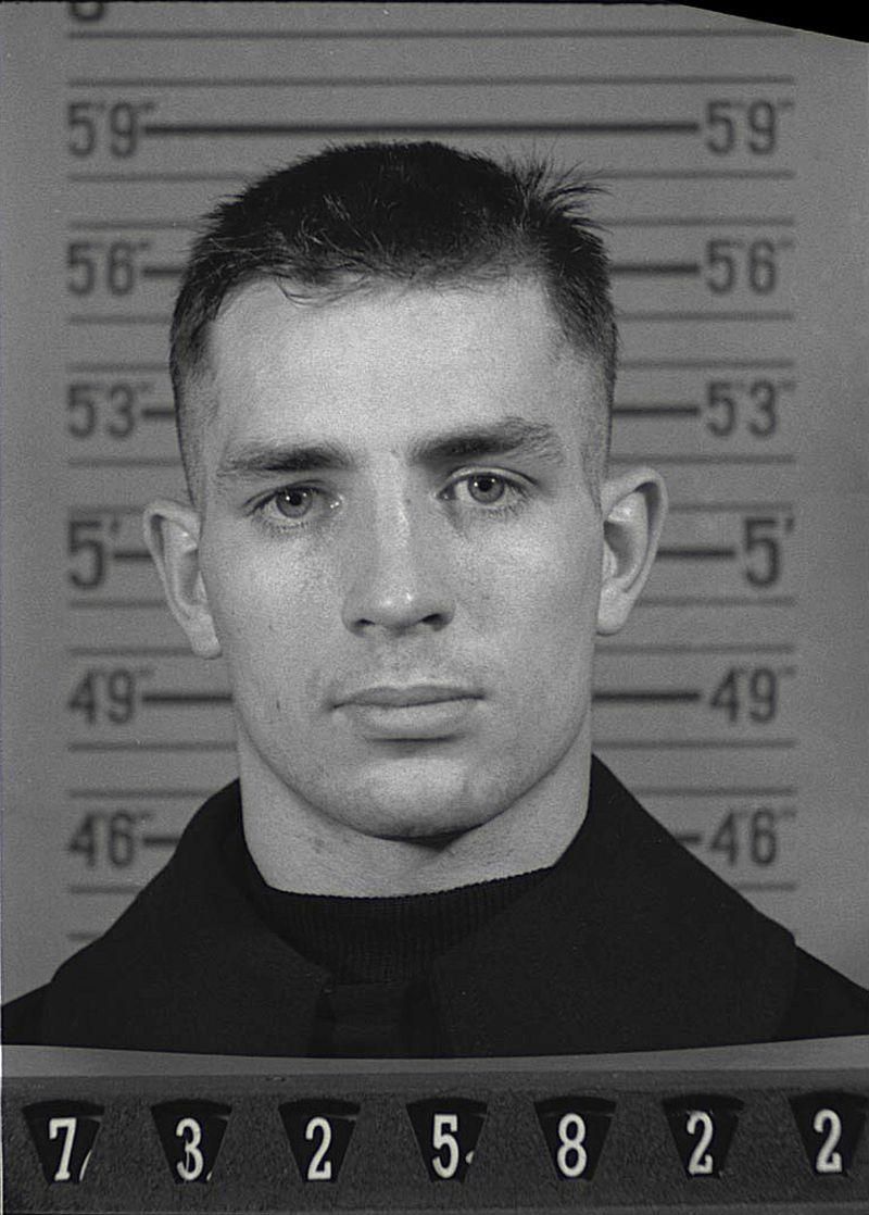 Naval Reserve Enlistment photograph of Jack Kerouac.- picryl.com. He standing in front of a height chart. (He is 5'9".)  At the bottom of the photo is his enlistment number.