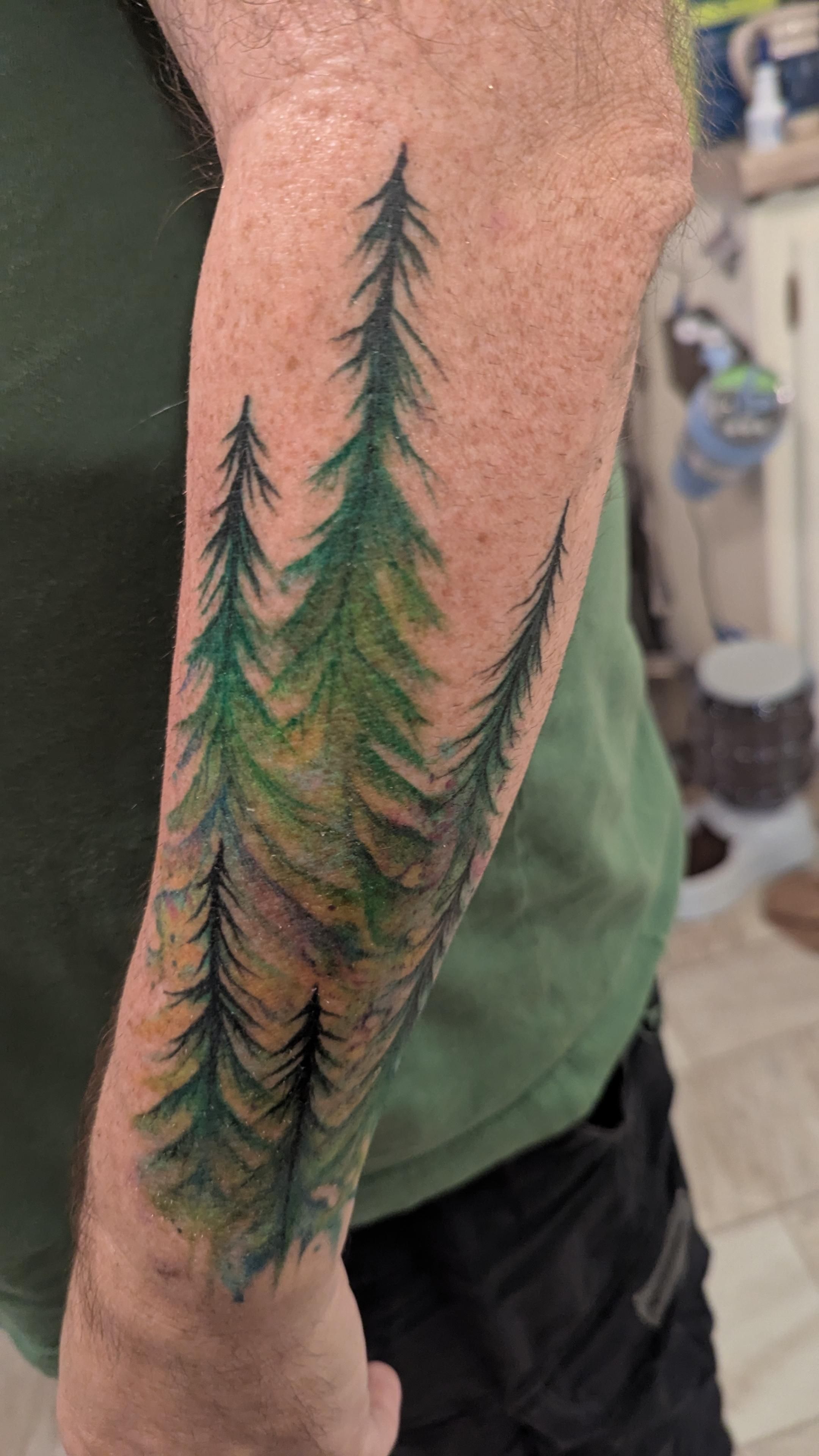 Forearm tattoo of trees in a green watercolor style.