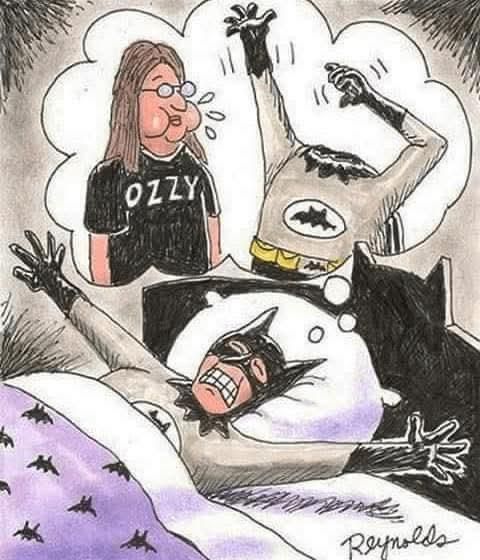 . Il personaggio di Batman è in posizione supina, con le braccia allungate e un'espressione di disagio sul viso. Sopra la sua testa, c'è un pensiero che mostra ozzy con i capelli lunghi e un paio di occhiali, indossando una maglietta nera con la scritta "OZZY". Accanto a lui, c'è un'altra figura che sembra essere un Batman senza il costume completo, con un'espressione di paura e le braccia alzate. La scena suggerisce che il personaggio di Batman sta sognando di aver perso la testa. Il letto è coperto da una coperta viola con disegni di pipistrelli,