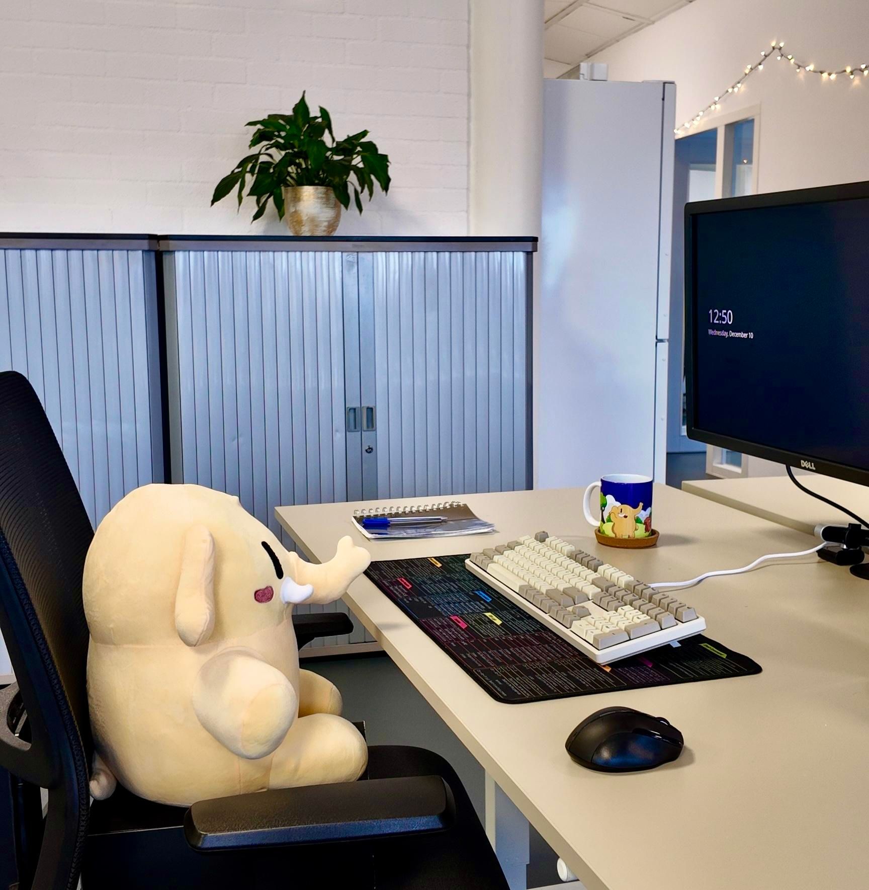 Een Mastodon knuffel die achter een bureau zit op een kantoor. 