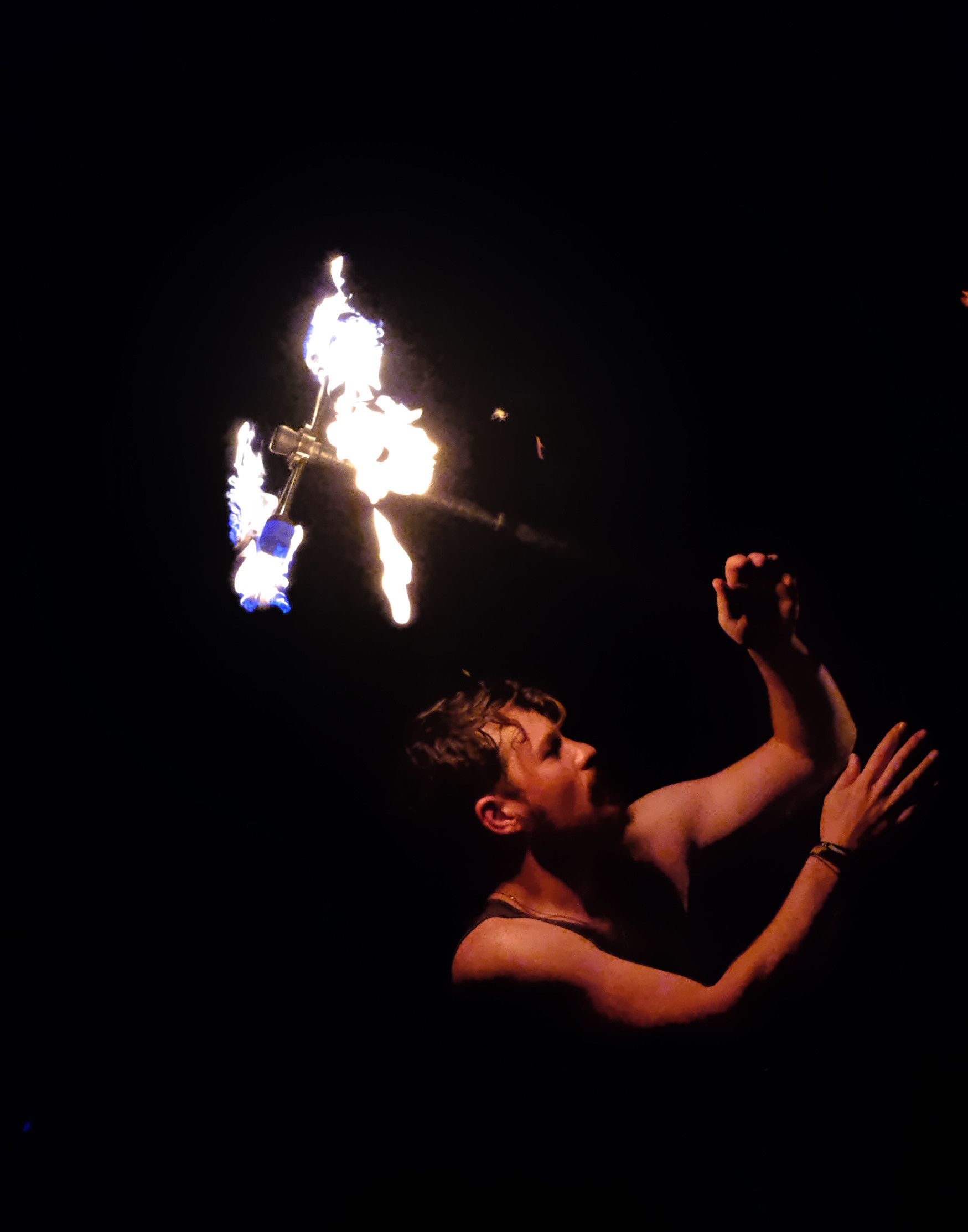 A man (apparently) in his 20s or 30s with a movie star face and hair, looking upward at his fire staff spinning over his head.