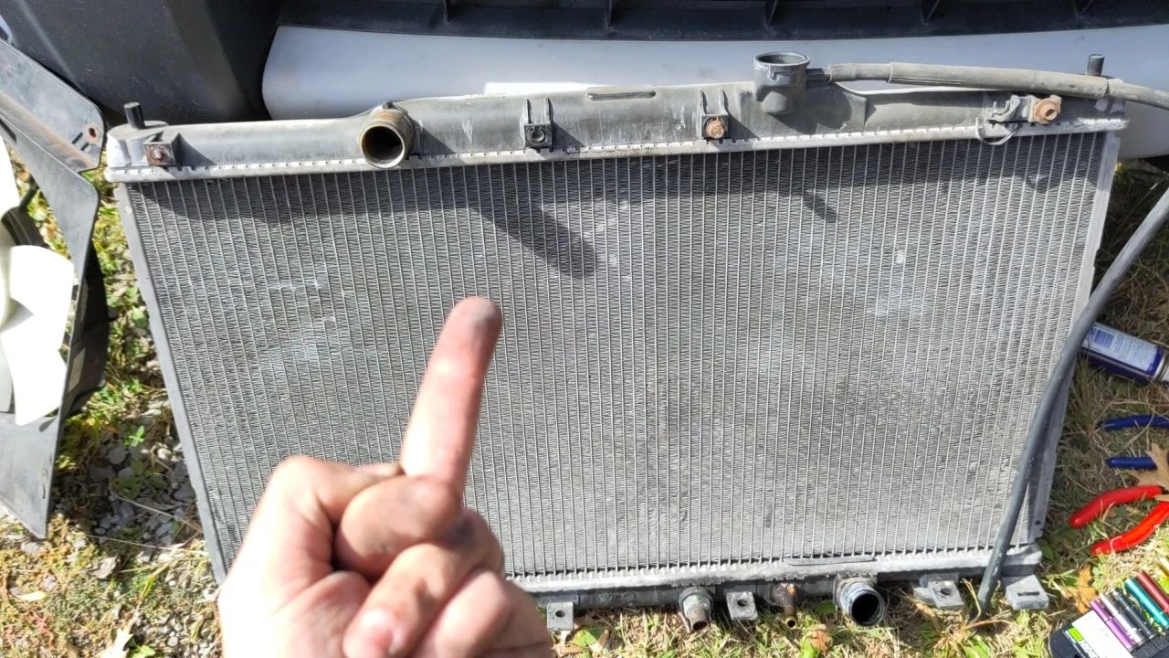 A busted Honda Element radiator, outside of the car. I'm giving it the finger