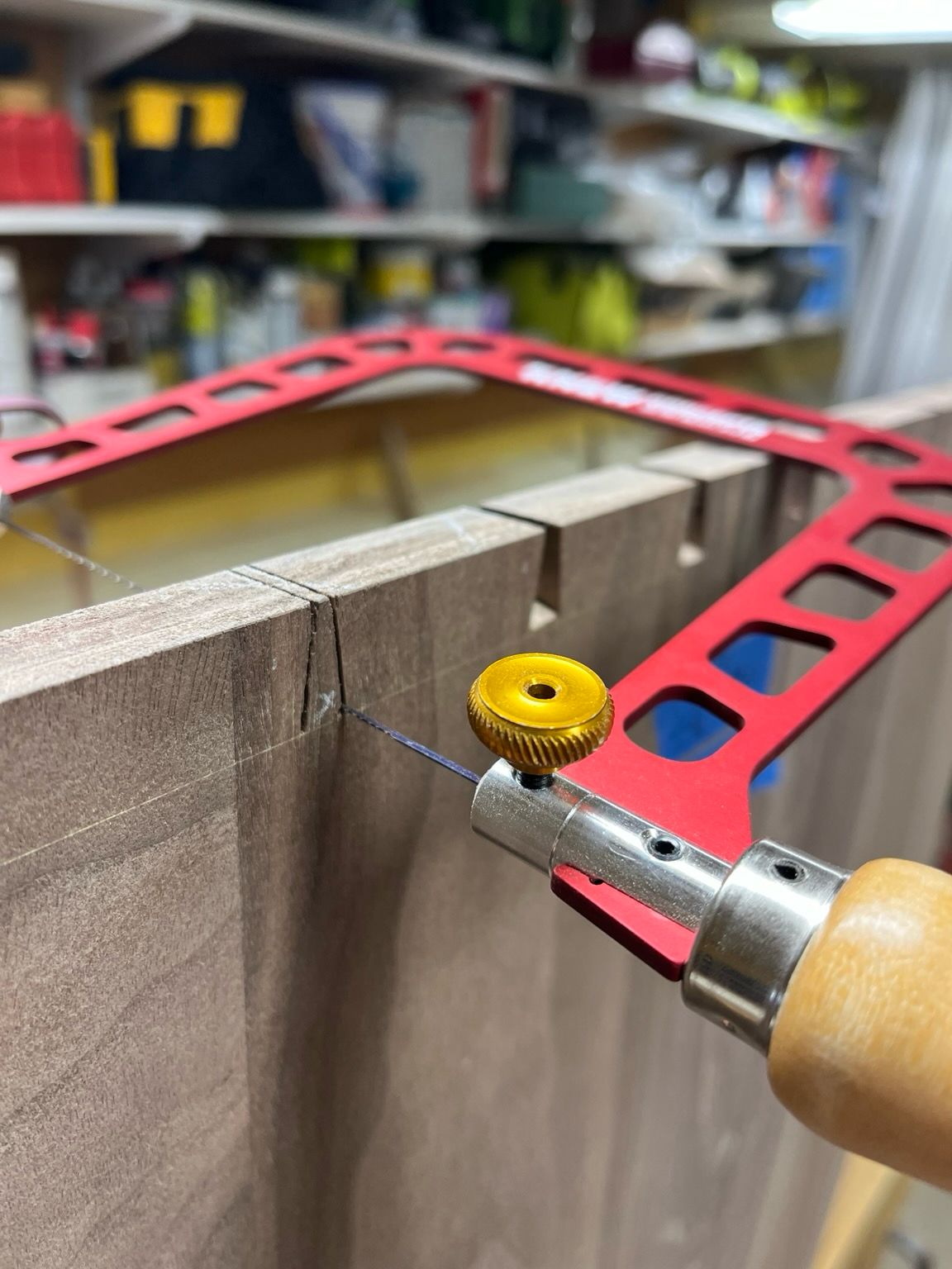 A red coping saw cutting the waste between dovetails in walnut wood.