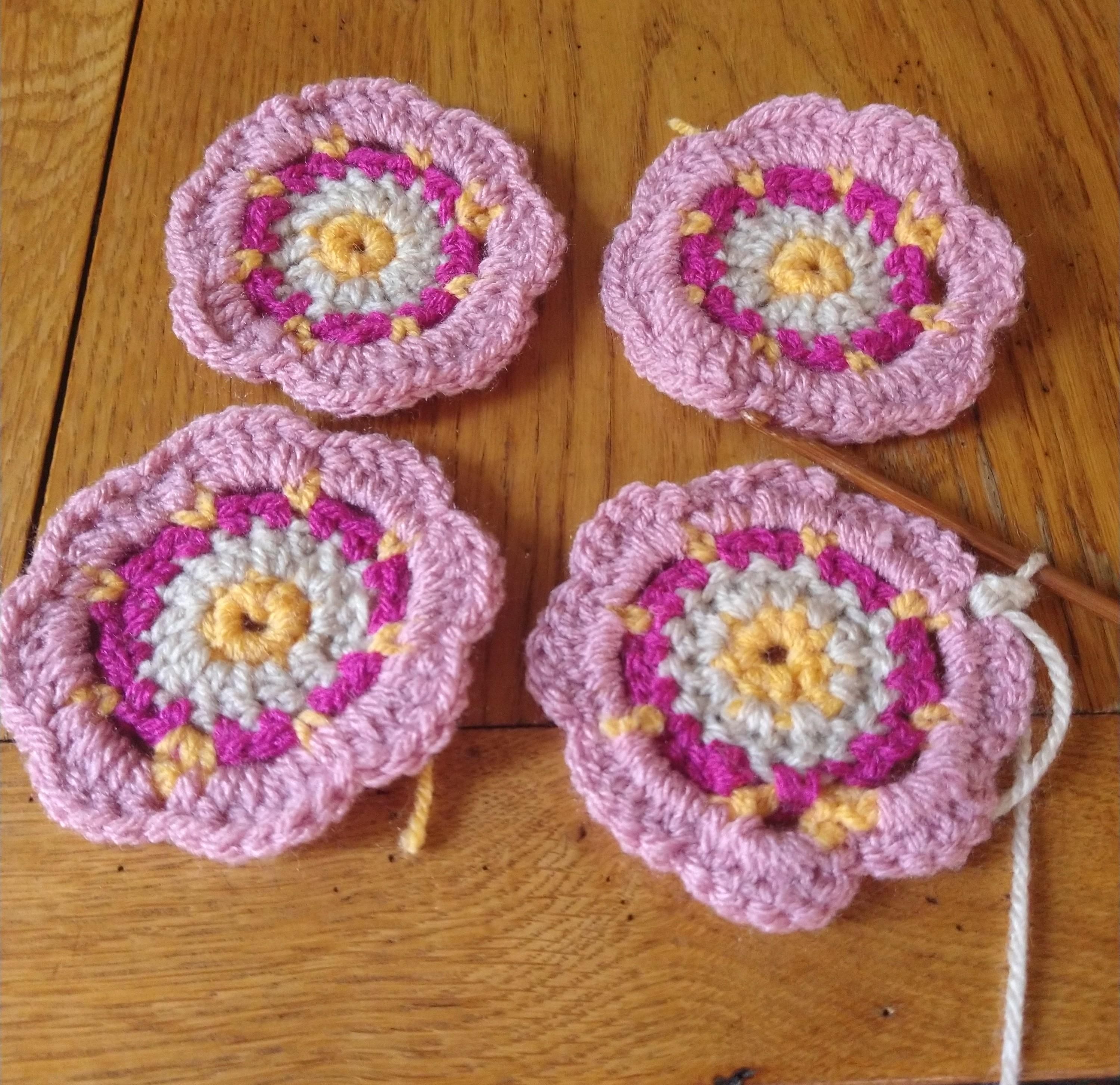 Four crochet motifs in pinks yellow and beige, looking like flowers which will be the central part of crochet squares 