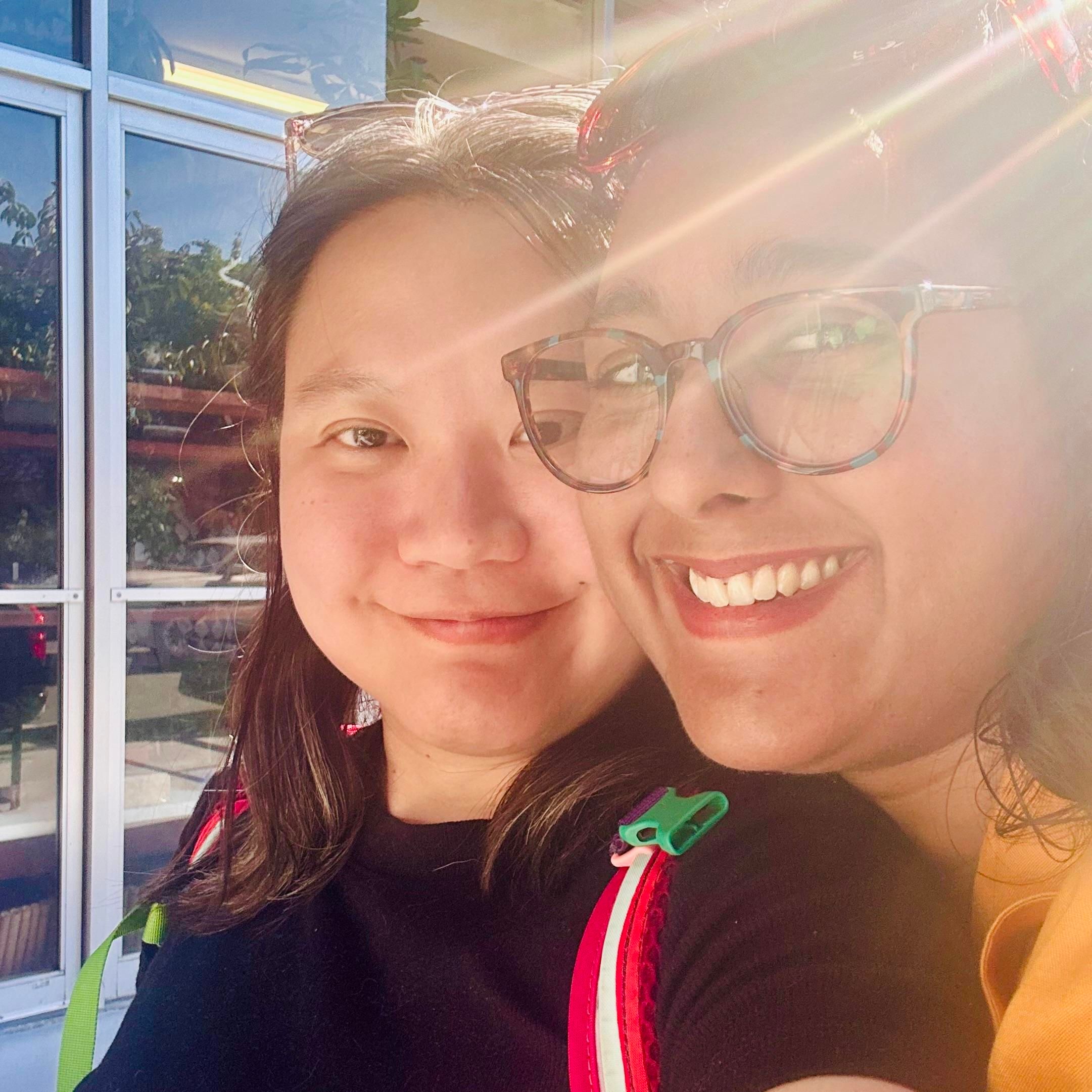 A selfie of two Asian women cuddling in the sunlight 
