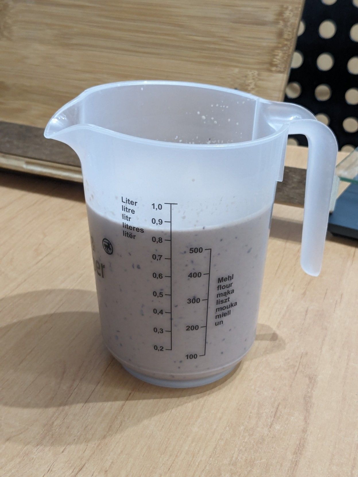 A 1 lt plastic measuring jar filled up to about 800+ ml with a beige milkshake that has some dark spots from the blueberries. It stands on a wooden table