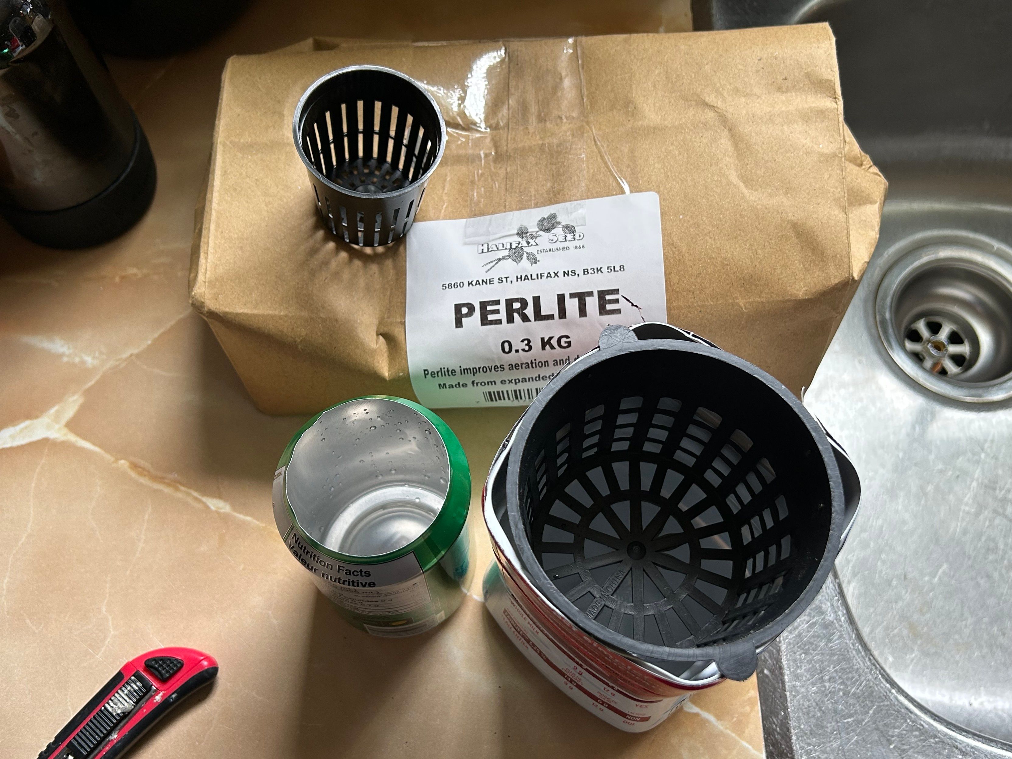 Image of the mesh baskets demonstrating their size, a pop can with the top cut off and a plastic milk carton with its top cut off, and a larger basket sitting neatly in it. A brown paper bag with the label Perlite is sitting beside it. 