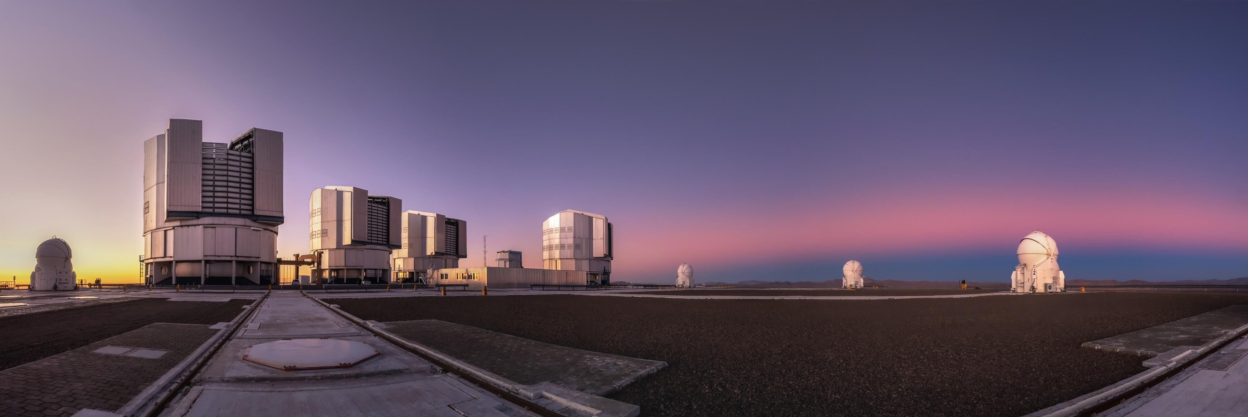 Before the night emerges, ESO’s Paranal Observatory glows in the colourful light of the Chilean sunset. Today’s Picture of the Week was taken by French photographer Julien Looten, who captured the Very Large Telescope (VLT) right as the Sun set, creating a pinkish band — the Venus belt. 

The Venus belt, unlike the name suggests, is not related to the planet Venus. It is an atmospheric phenomenon caused by the scattering of the Sun’s light when it either rises or sets, visible on the opposite side of the sky. As sunlight reaches the far end of the atmosphere, small particles scatter it back towards the observer, creating a pinkish band. The dark band right below it is the shadow of the Earth cast on to the sky as the Sun sinks below the horizon on the opposite side. 

Looten caught this moment in a panorama right after sunset, before the arrival of the night when “the excitement was at its peak”, he explains. The same way the photographer prepared to capture the clearest night skies above the Chilean Atacama Desert, the telescopes of the Paranal Observatory got ready to observe the mysteries of the cosmos. 

Credit: J. Looten/ESO
