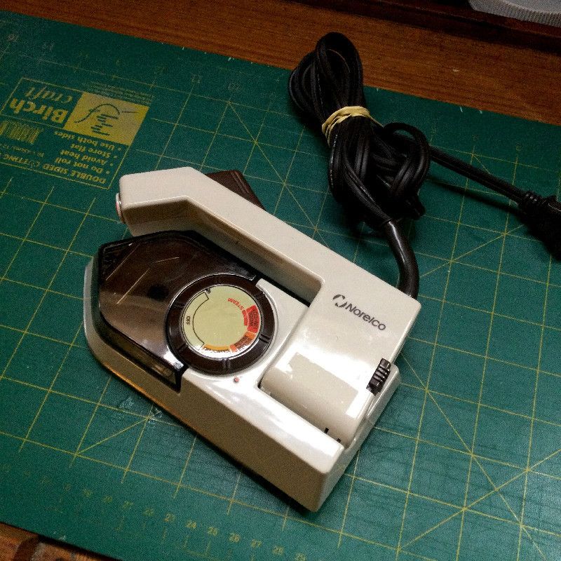 a model TI-70 Philips steam iron laying over a cutting board. The cord is bound by an elastic band. The steam iron handle is folded down.