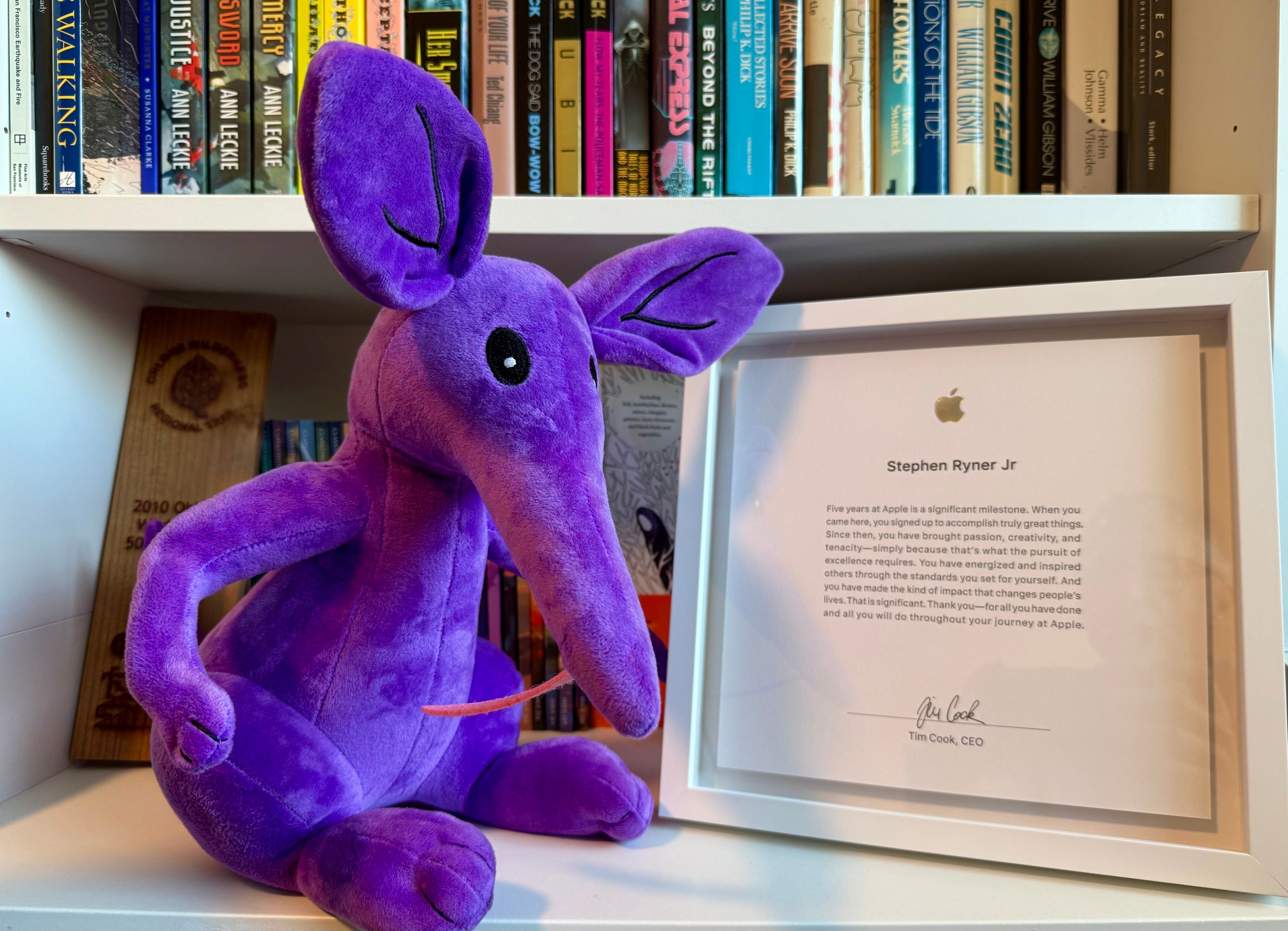 Photograph of an Apple five year anniversary plaque. A purple aardvark plushie sits beside the plaque. Anika is the unofficial mascot of Radar, the system Apple uses for tracking features and issues.