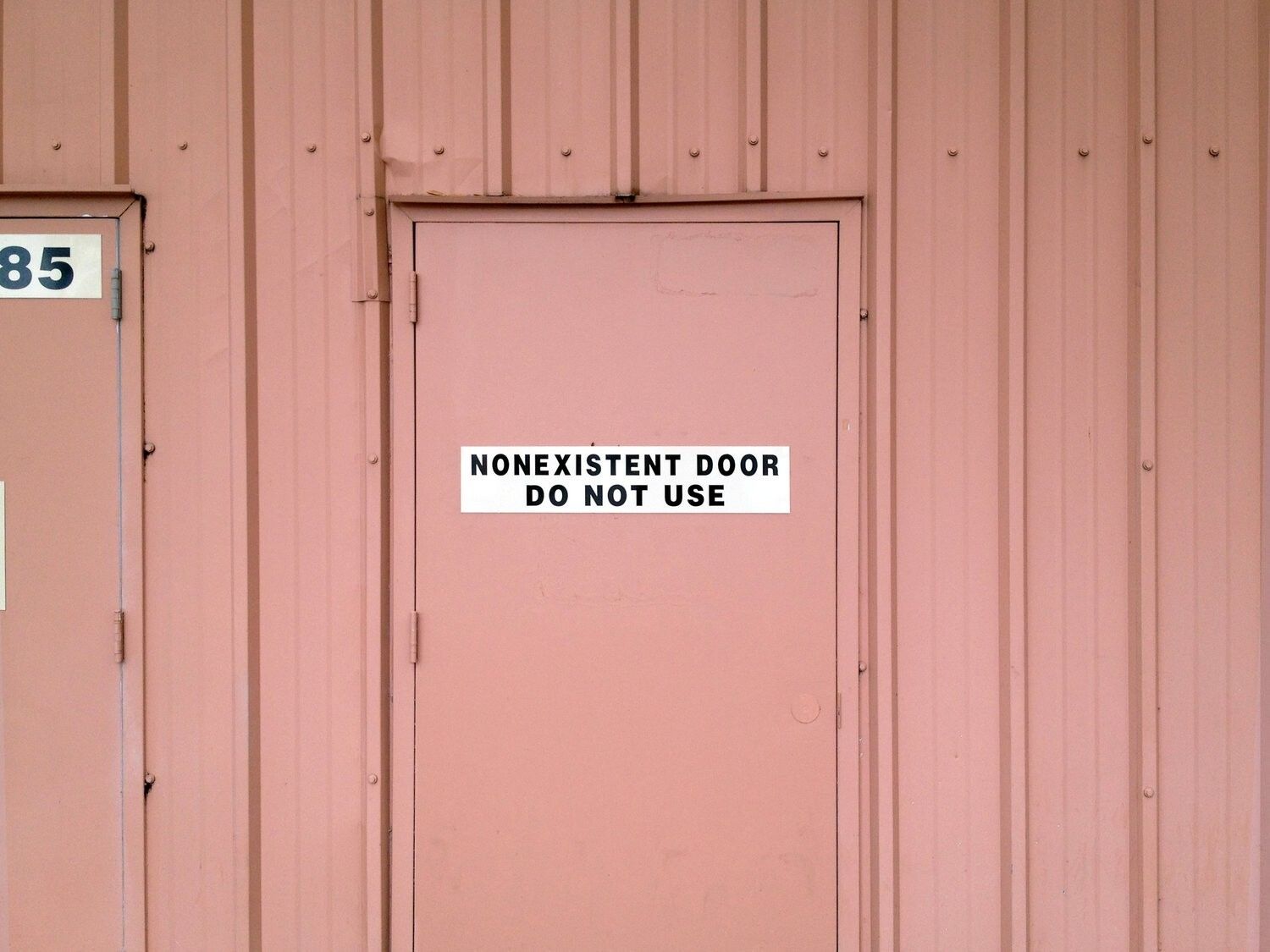 a pink door in a pink wall with a white sign with black text saying "nonexistent door do not use"