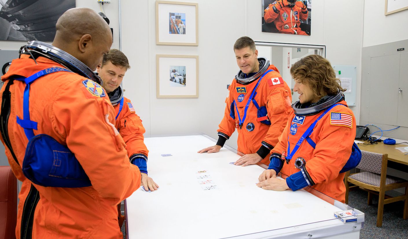 Four Artemis II astronauts stand, with two on each side of a planning table.  At the back is the Canadian astronaut Jeremy Hansen with a maple leaf on his shoulder