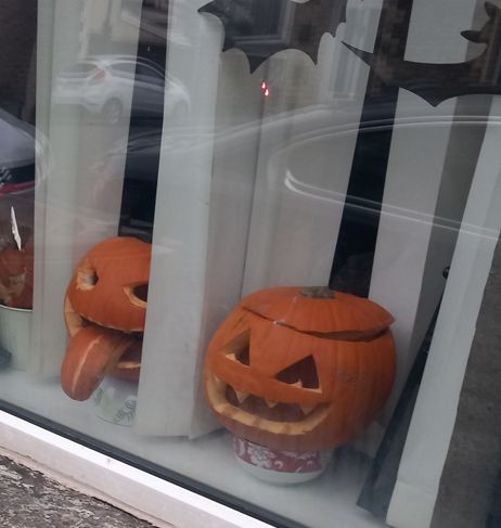 Two carved Halloween pumpkin heads on a windowsill, one with part of the rind sticking out of the mouth like a tongue.