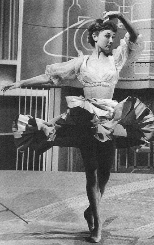 Audrey wears a tutu and twirls, one arm above her head. 