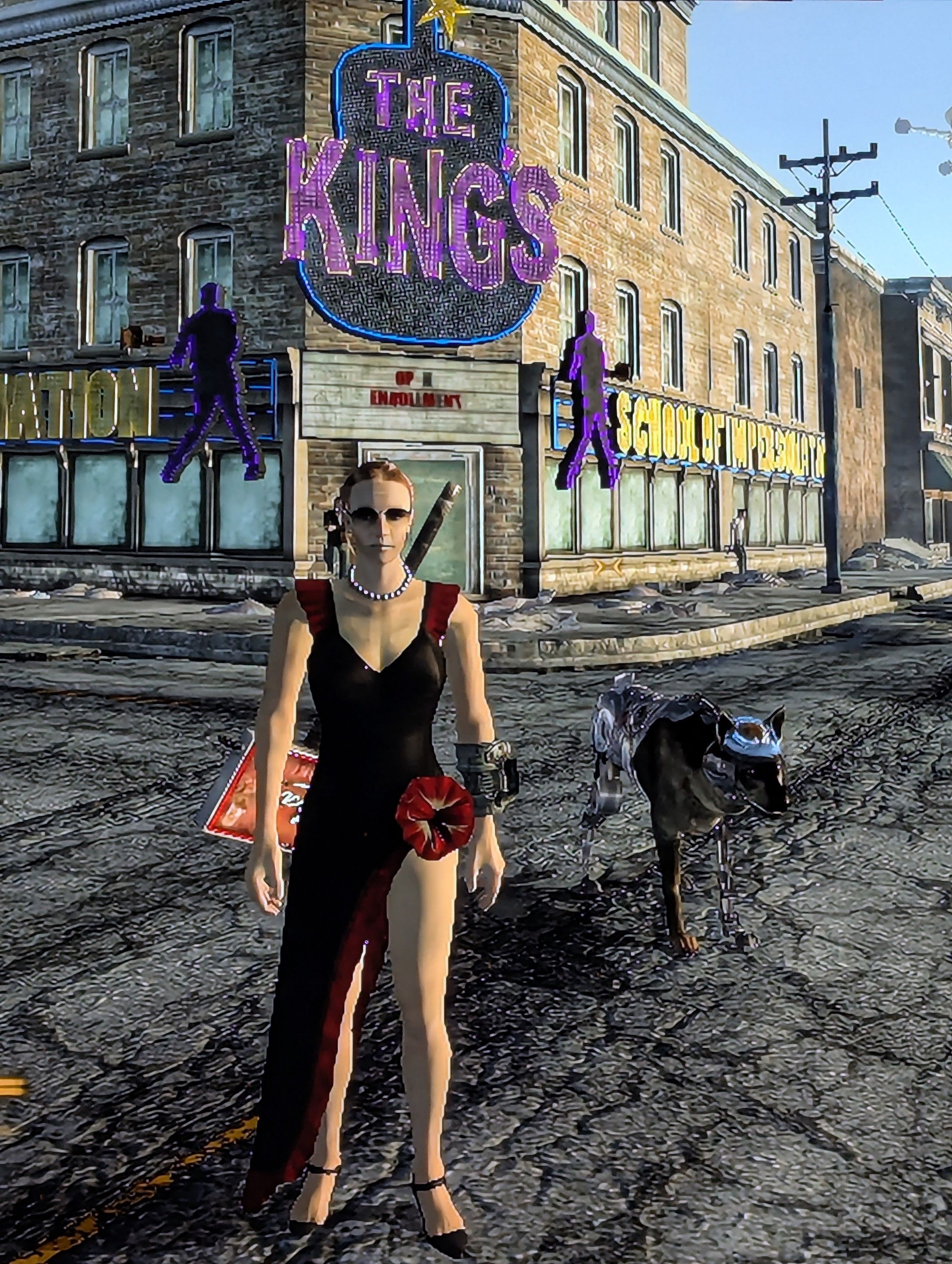 Fallout New Vegas game image of the player character, a white woman in a flamenco dress with a person necklace and aviator shades. She has a store display sign holstered on her back. She has a robot dog with visible brain next to her. They stand in the middle of an intersection in from ofs building with a purple sign that says THE KINGS with silhouettes of Elvis on either side. The street and sidewalks are broken because it's 200 years after the nuclear apocalypse.