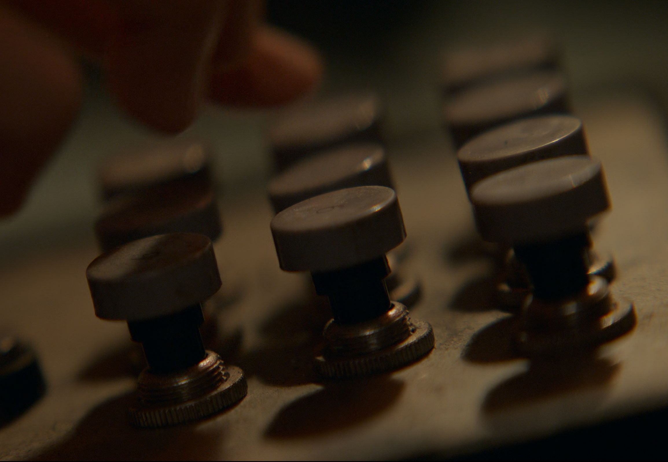 Screenshot from the show. Three rows of buttons and a hand over them. Each button has a round "keycap" and a dark, tall, cylindrical stem inserted in grey metal "ring" with parallel ridges.