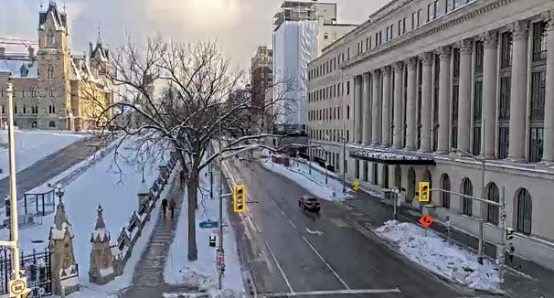 A portion of the Parliamentary East Block to the left and monumental buildings to the right of the view.  Mostly empty streets and sun catching parts of the stone buildings.