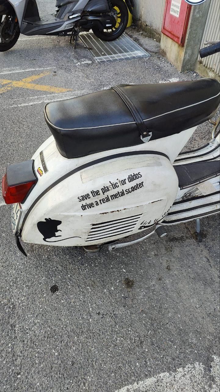 Vespa Piaggio bianca con scritta sulla scocca laterale destra: "save the plastic for dildos - drive a real metal scooter"