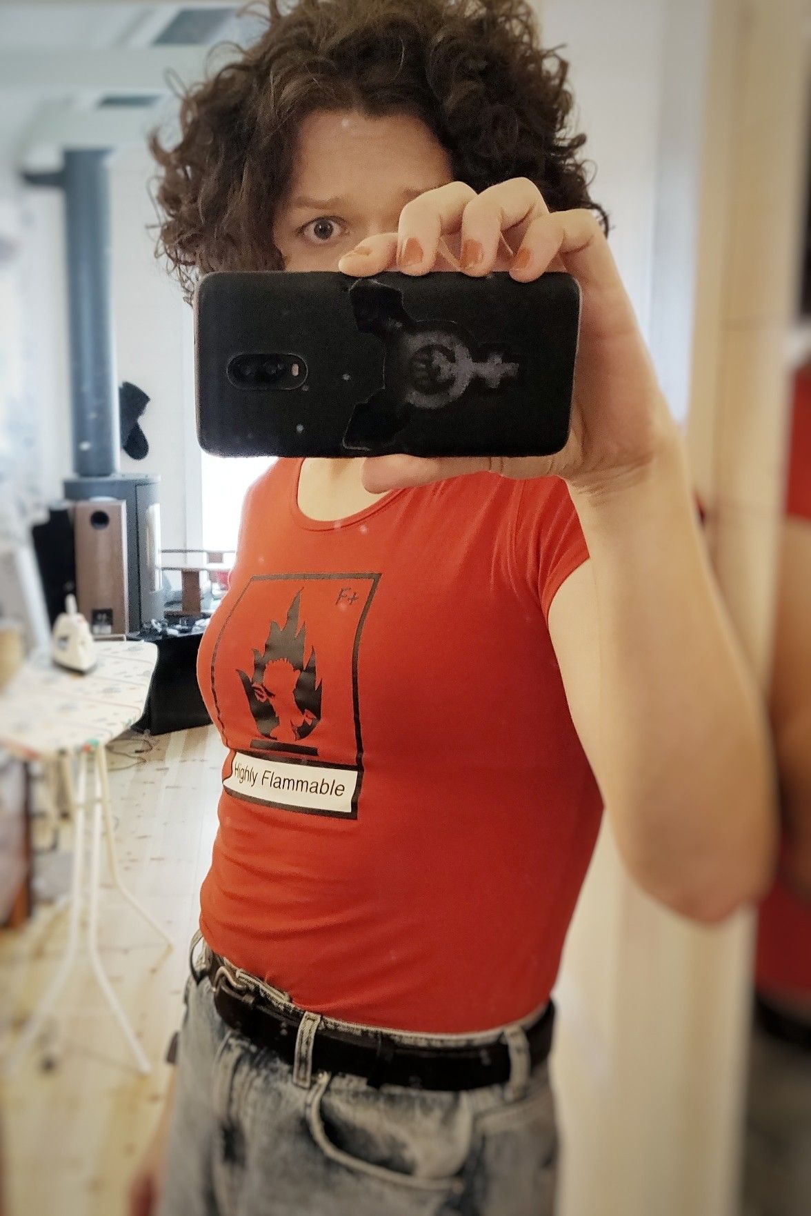 A concerned eye is seen behind my phone, and beneath it in a tight red top I have boobs. The top says “highly flammable”.
