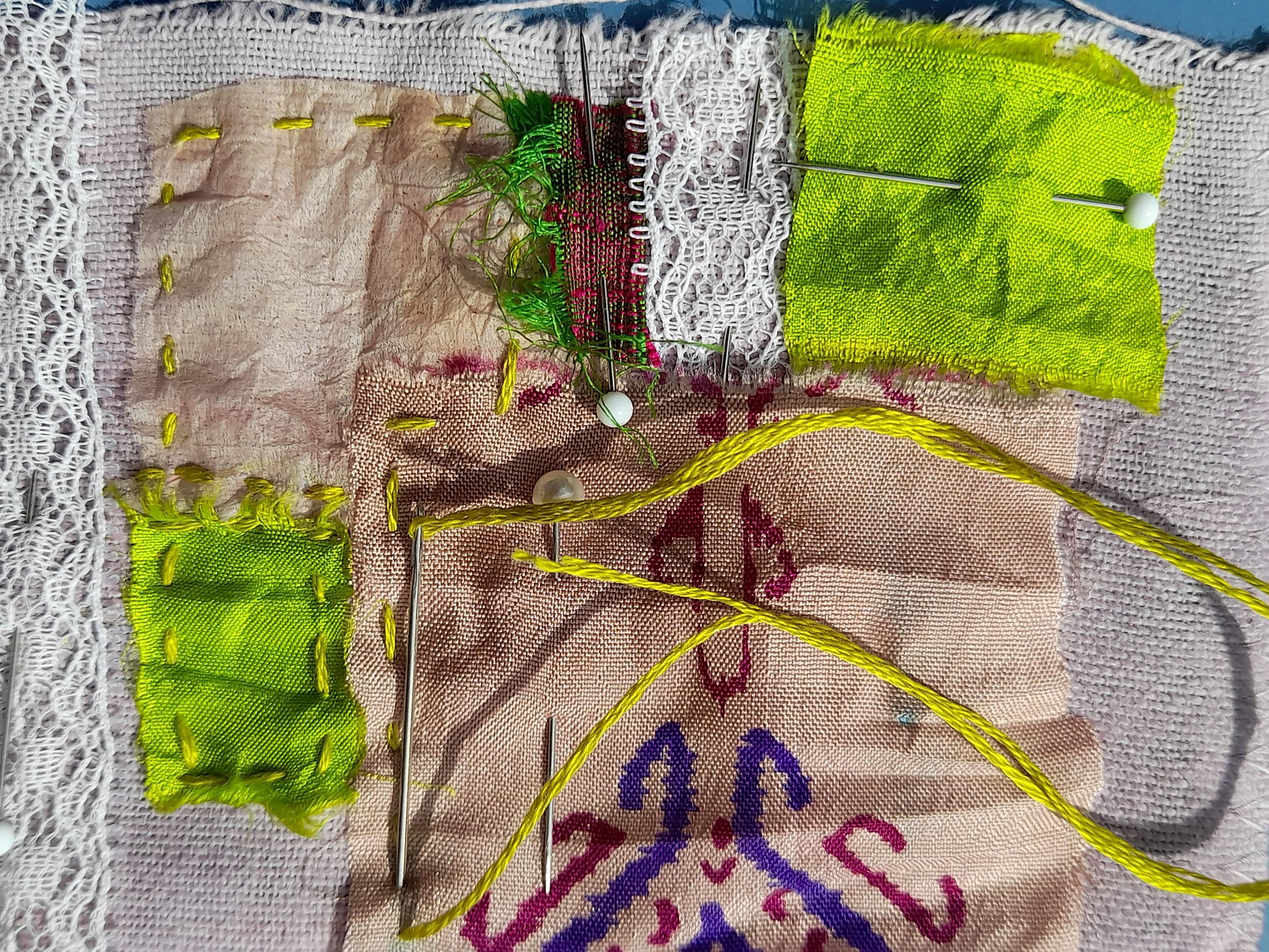 Part of my scrollbook with a needle and yellowish green thread. On a background of bright purple flannel a collage of small white lace, a square of a used teabag and scraps of saree silk. The spuares and rectangles are laid in a collage composition and get fixed with wild, wobbly stitches. One silk scrap in rosé has a beautiful dark lilac and red ornamental print.