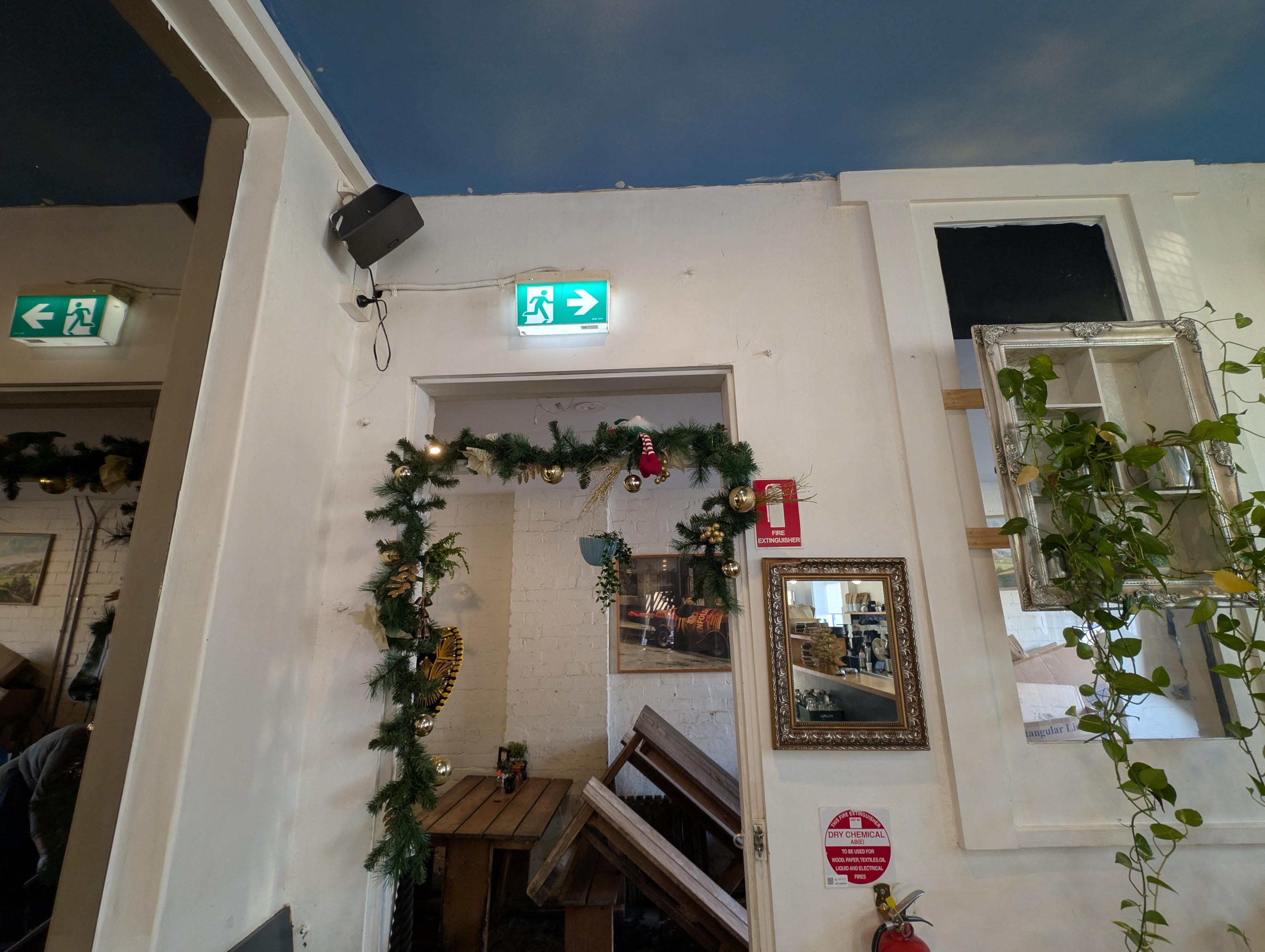 The elf is sitting above the door, which has Christmas decorations around the frame. To the right is a shelf with vines ground around it