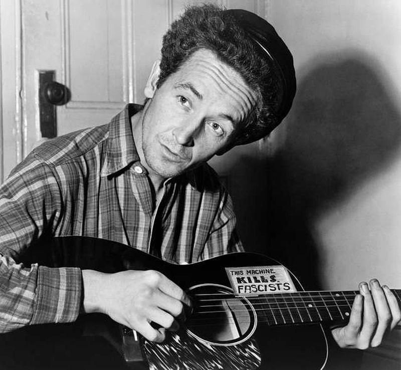 "Woody Guthrie, half-length portrait, seated, facing front, playing a guitar that has a sticker attached reading: This Machine Kills Fascists" - picryl.com