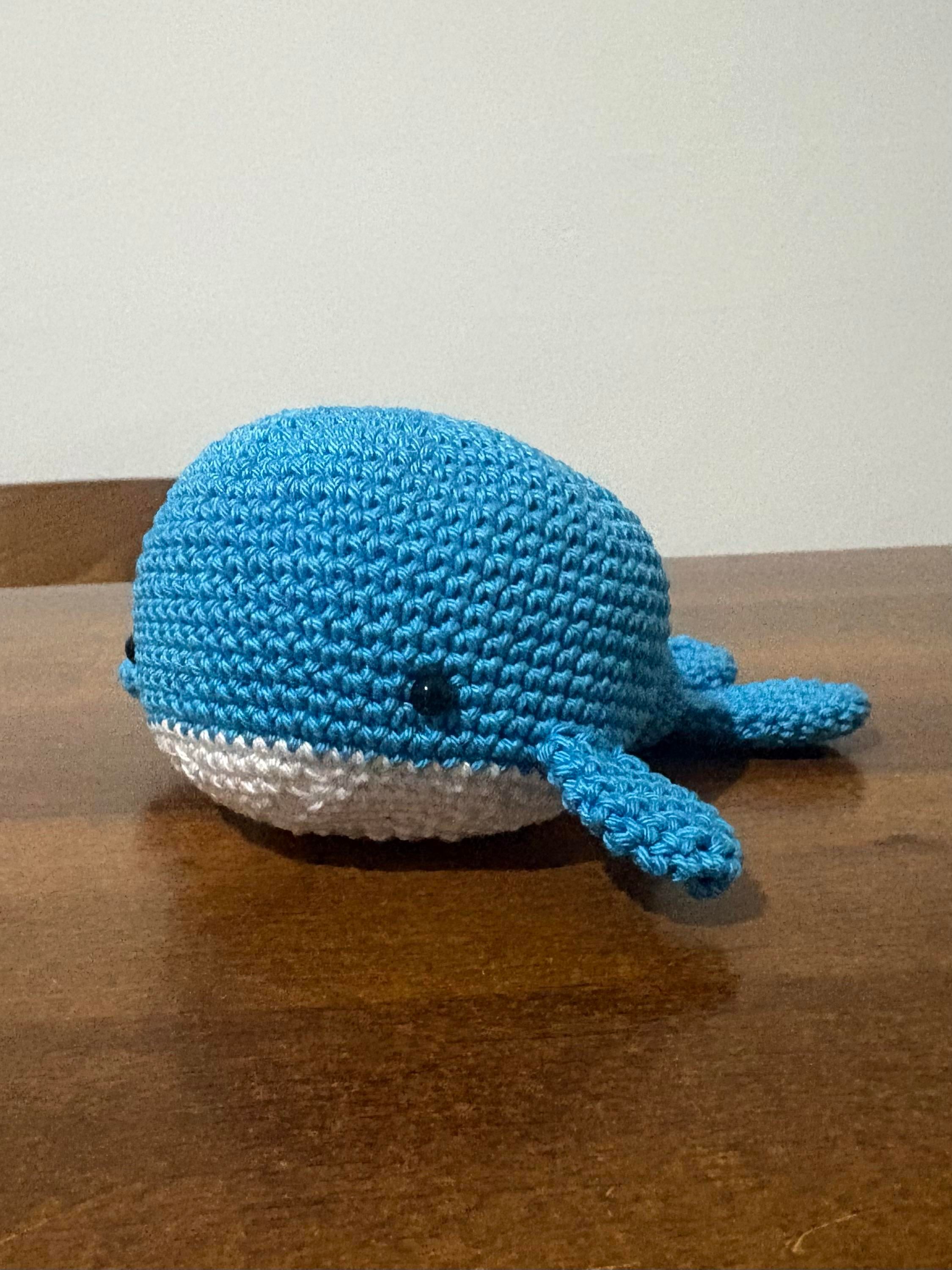 Primo piano di una balena amigurumi fatta all’uncinetto con dorso azzurro e ventre bianco