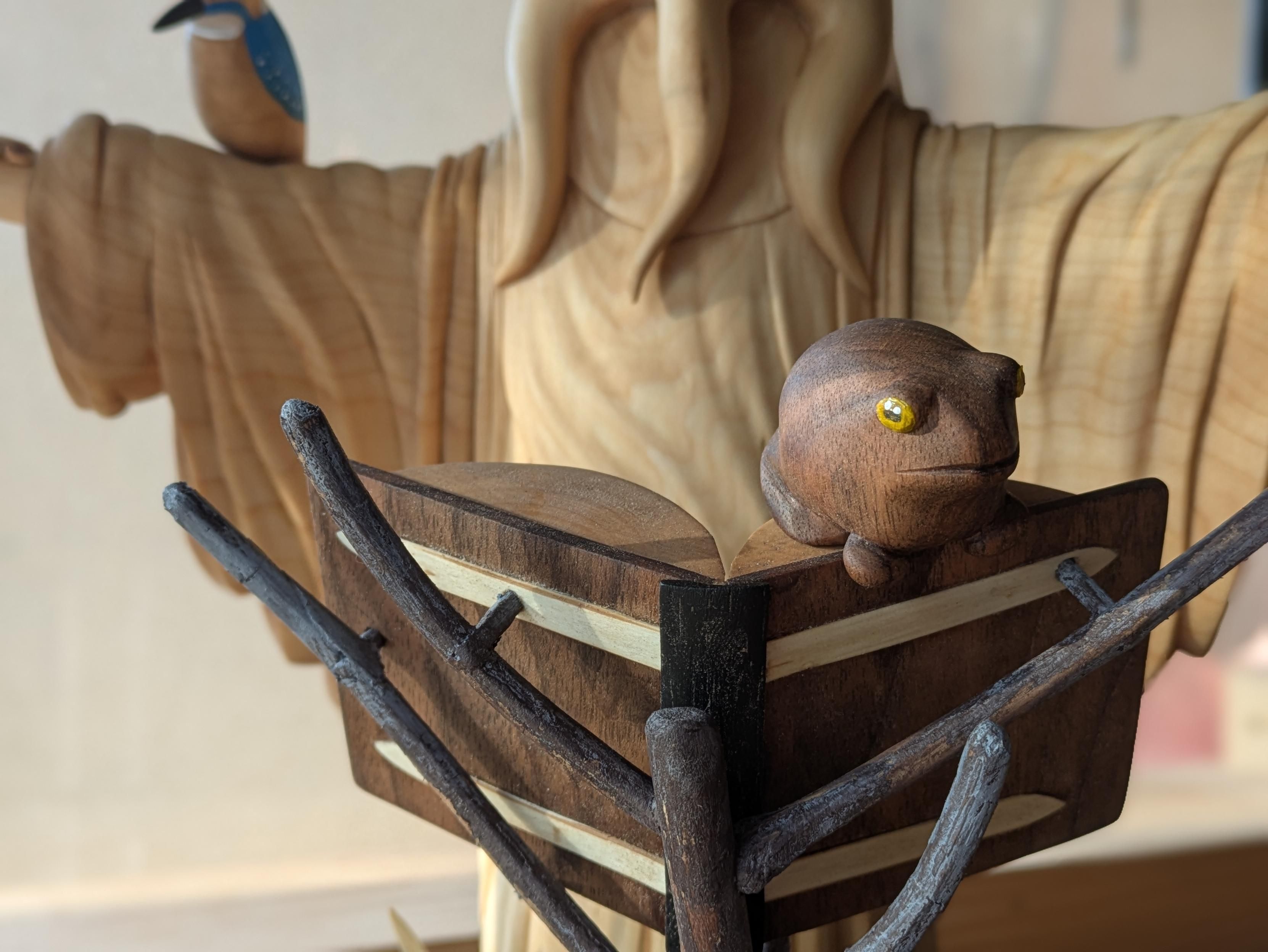 Woodcarved scene, focus on a frog sitting on a book, that is hold by branches