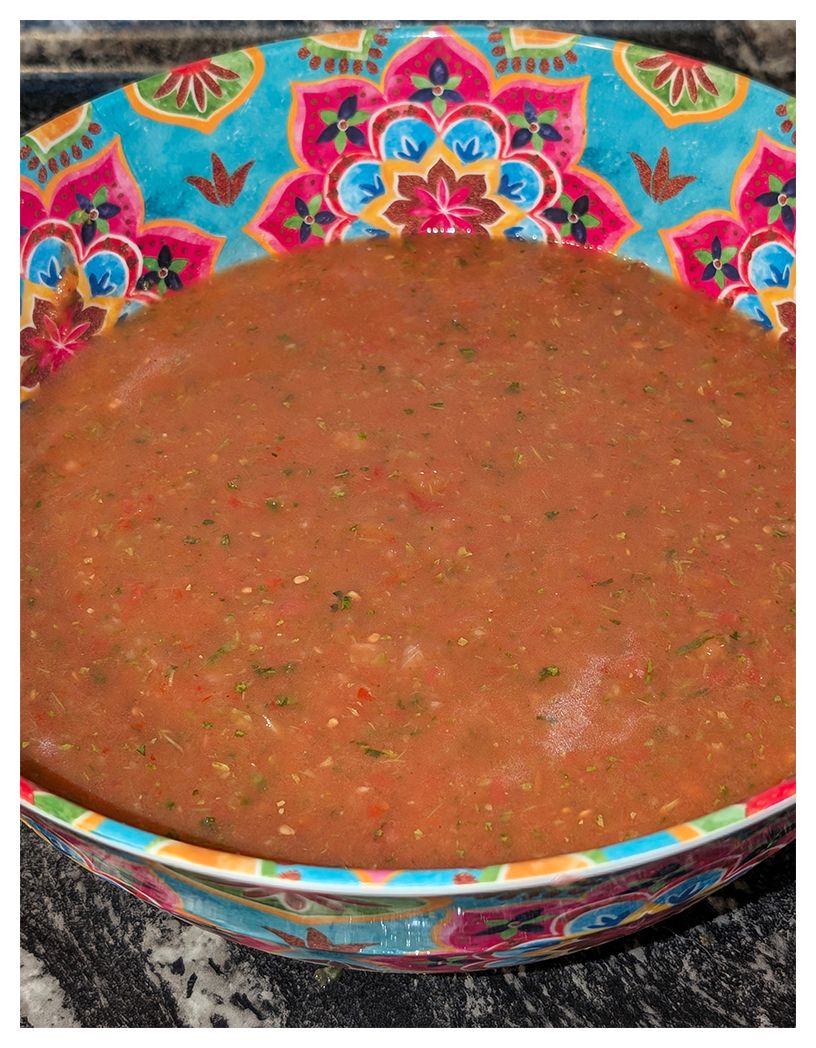 large bowl with mandala design sits on marble counter and is half-full of red soup with flecks of red, green and white.