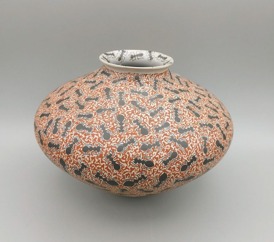 A very fine painted decorative "Mata Ortiz" vase made by Guadalupe Gallegos. It is very smooth and wide with a narrow opening at the top. The motif is ants on a red background. They also cluster enthusiastically around the white rim. 