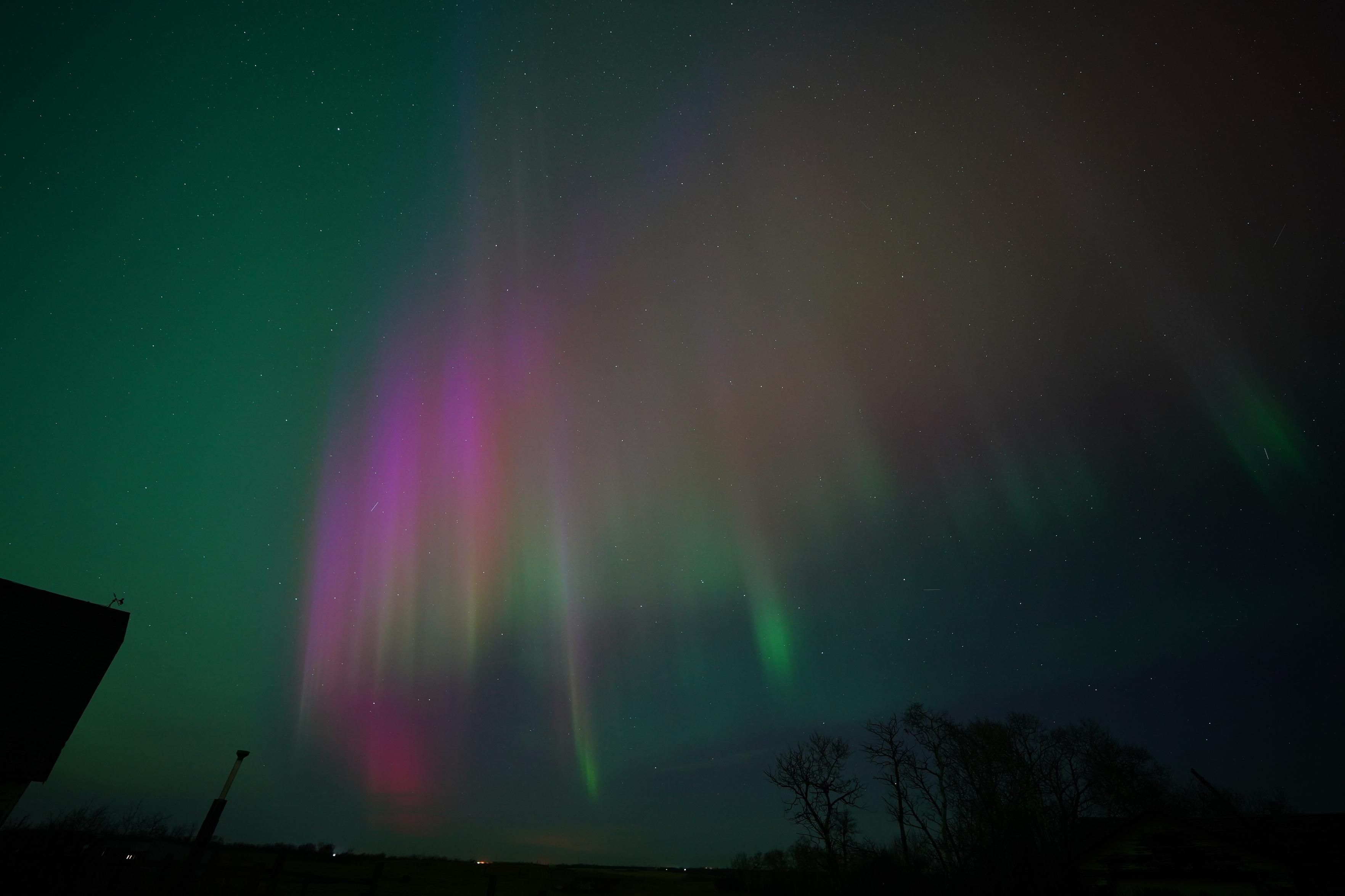 A bunch of columns in an arc, but a few of the columns start lower down in the sky, and are bright green at the bottom.  All of the columns transition to orange and then red and the purple.  The rest of the sky is green.