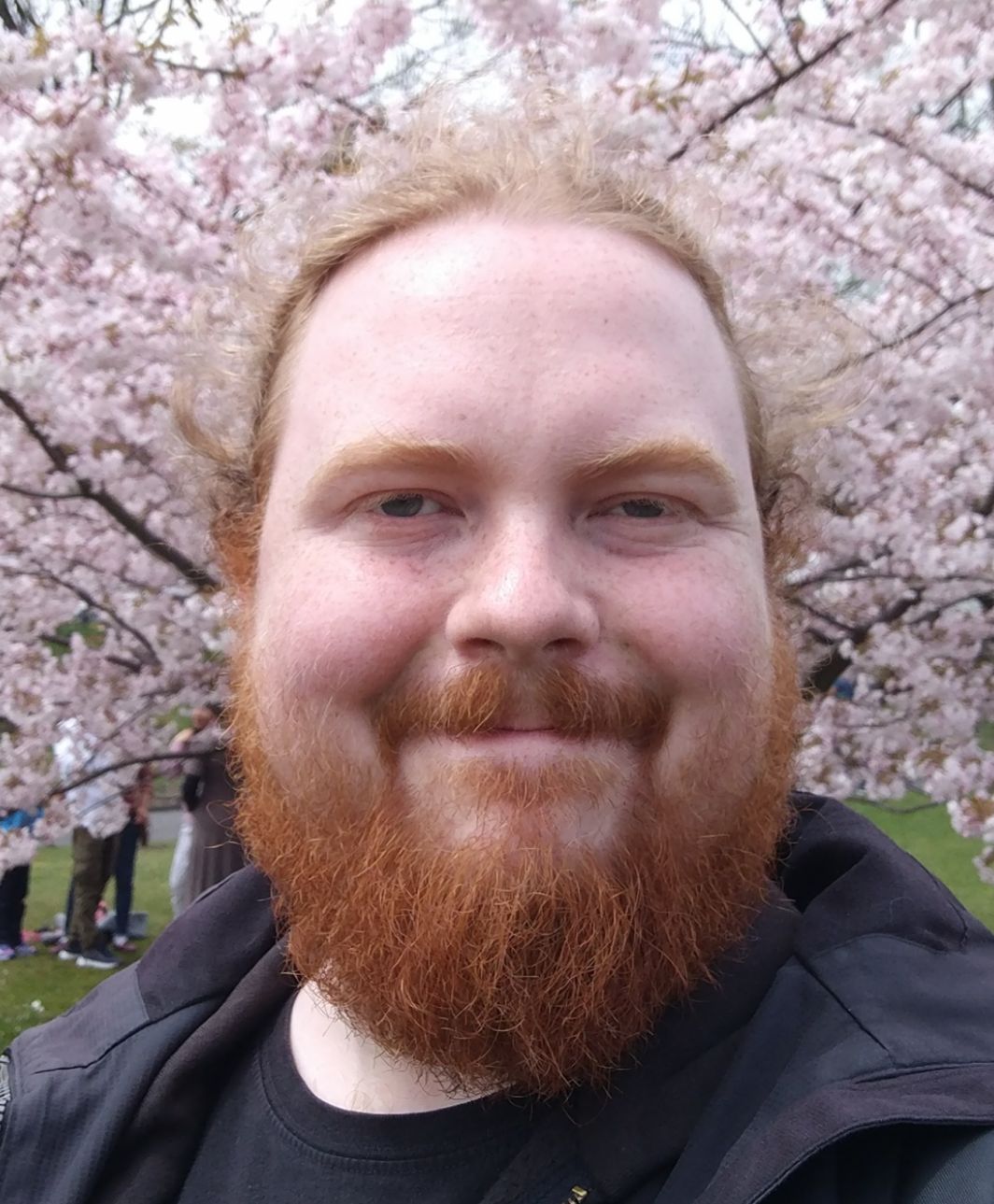 My face is pretty round, especially the cheeks. And my beard is longer! The photograph is taken in front of a blooming cherry tree.