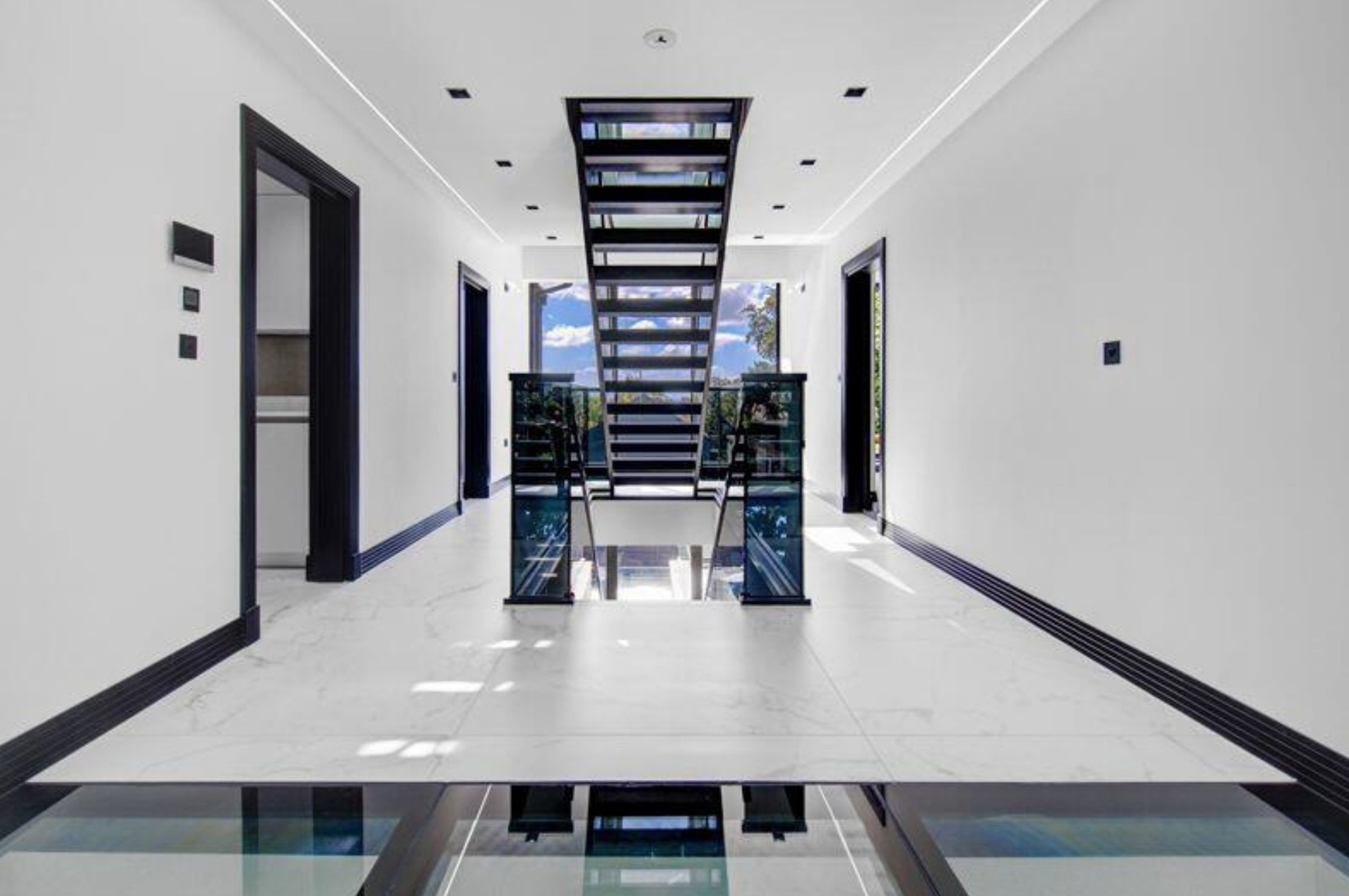 A hallway with stairs going up into the middle, but it looks like the floor is suspended above another floor that is glass and you can see through it. 