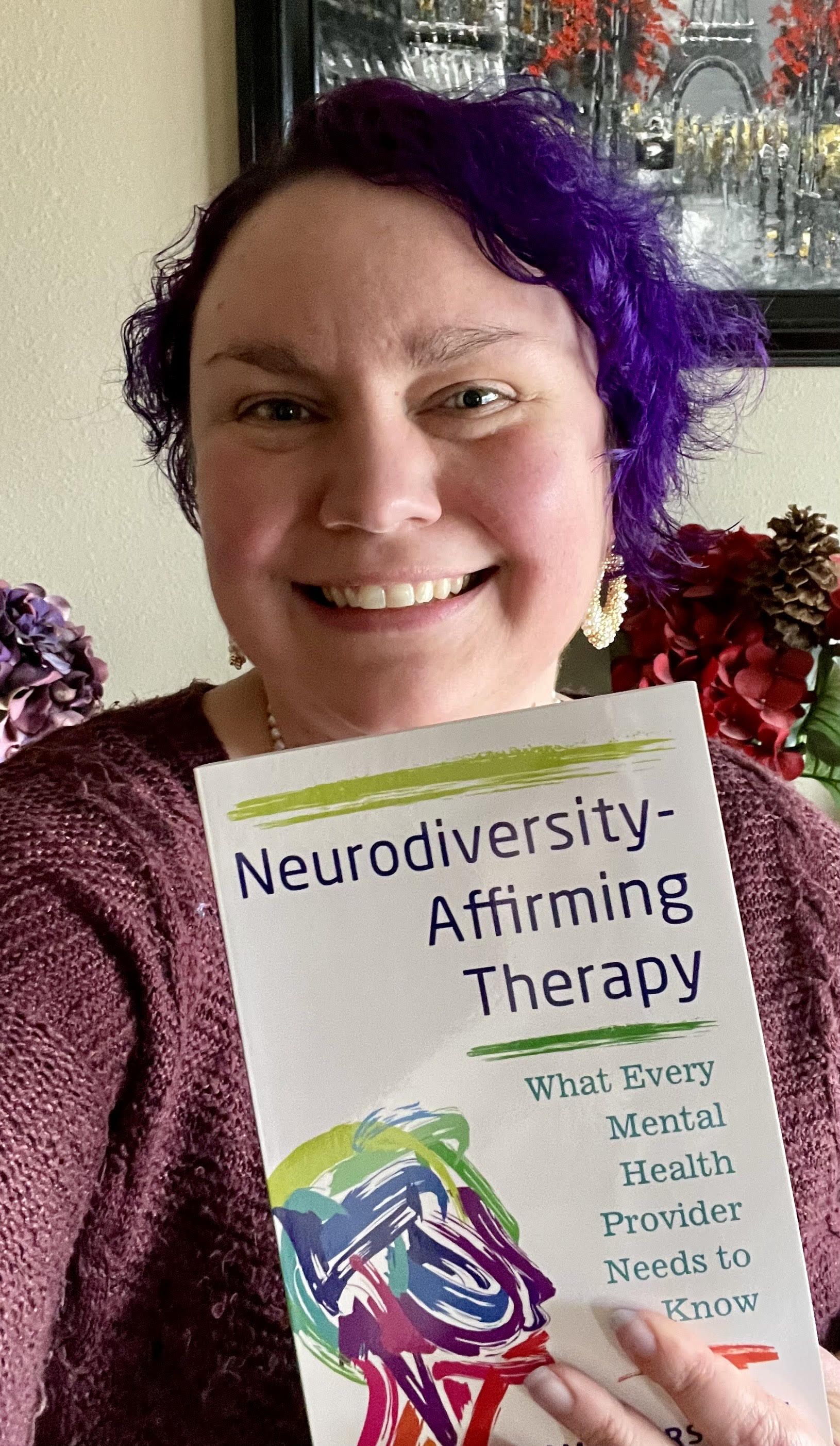 Selfie, I am holding up a copy of my upcoming book Neurodiversity-Affirming Therapy: What Every Mental Health Provider Needs to Know.