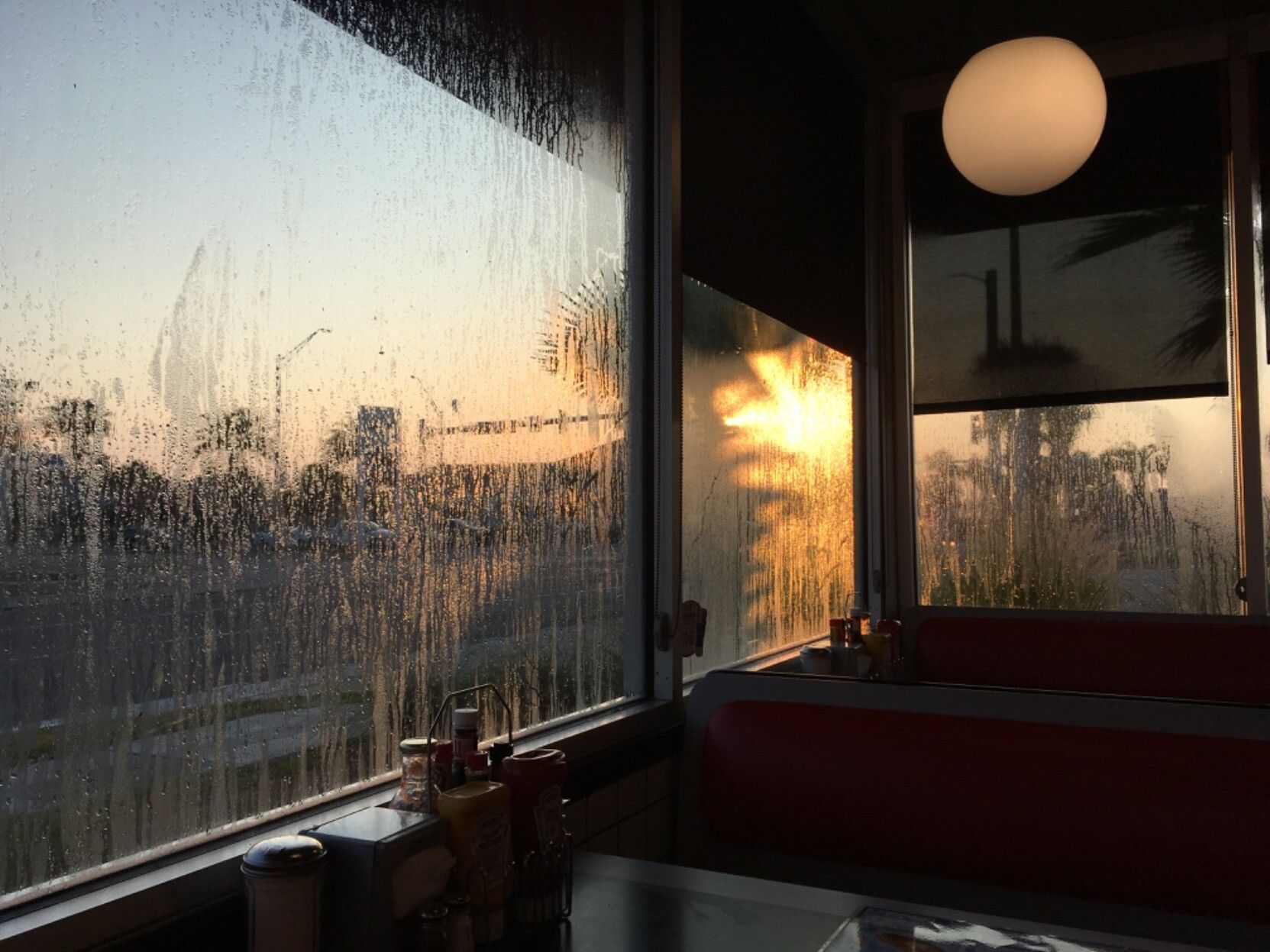 View from a booth at Waffle House just as the sun is rising. It’s near the beach and you can see palm trees through the windows. The condensation on the windows is golden with the sunlight. This is the purest form of Waffle House 