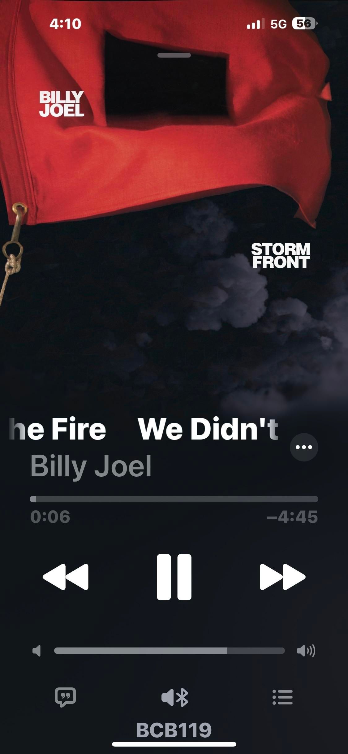 The image displays a music player interface featuring the song "We Didn't Start the Fire" by Billy Joel, set against a background of a red flag. The title "STORM FRONT" is visible, along with the track duration and playback controls at the Max