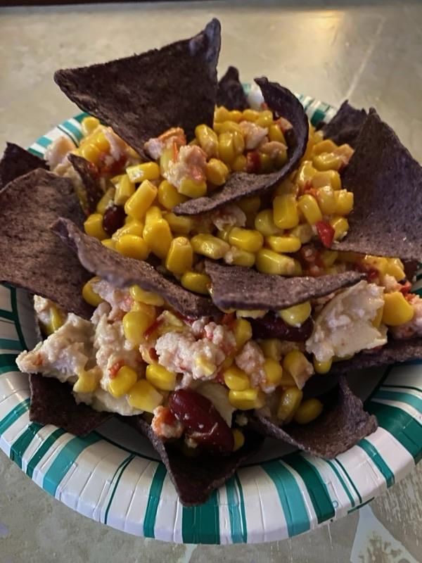 close up of bowl filled with a mixture of corn and chicken salad and blue corn chips tucked in around the edges and centre